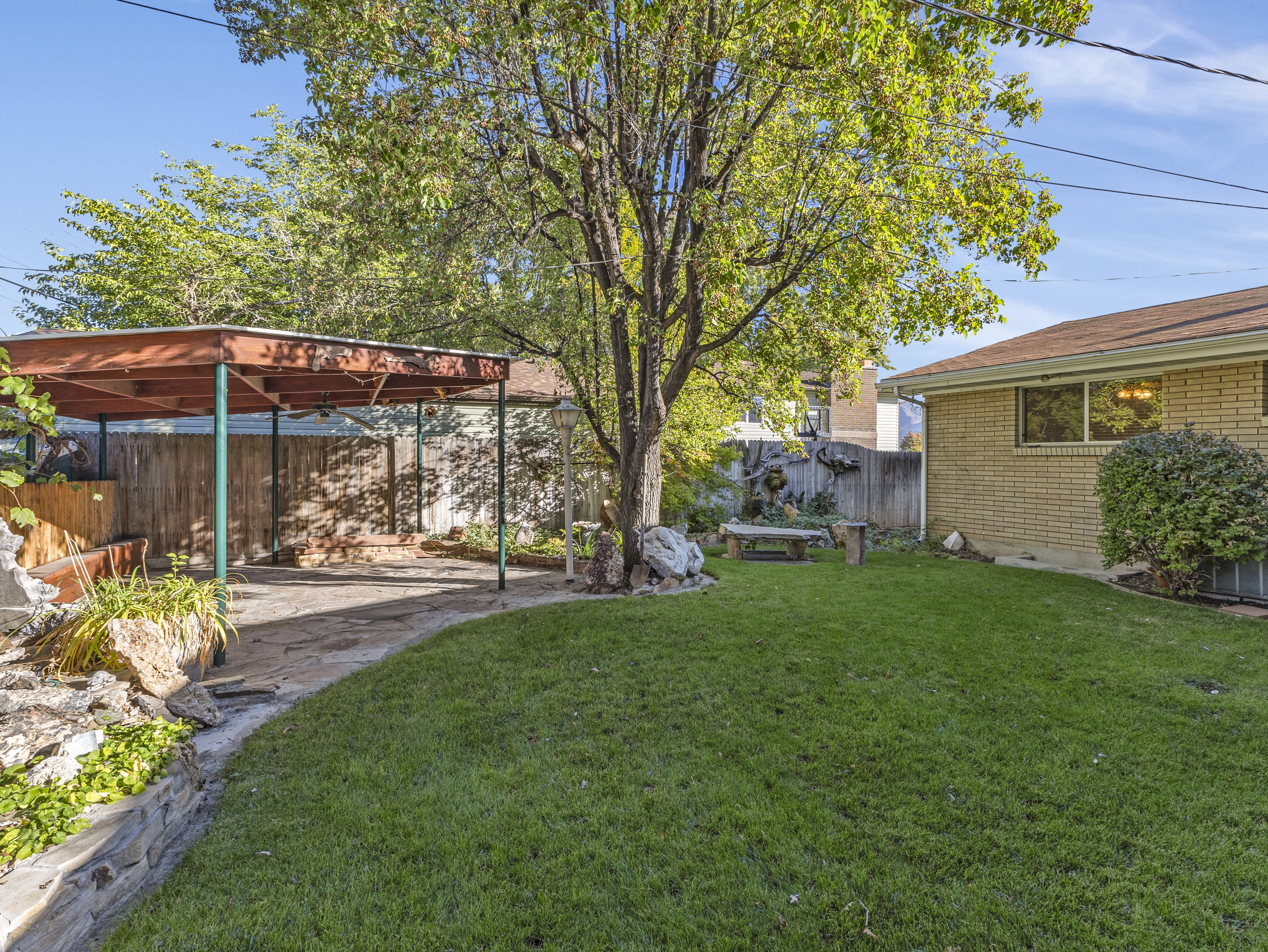 Expansive backyard featuring a covered patio, established tree, manicured lawn, and perimeter fencing