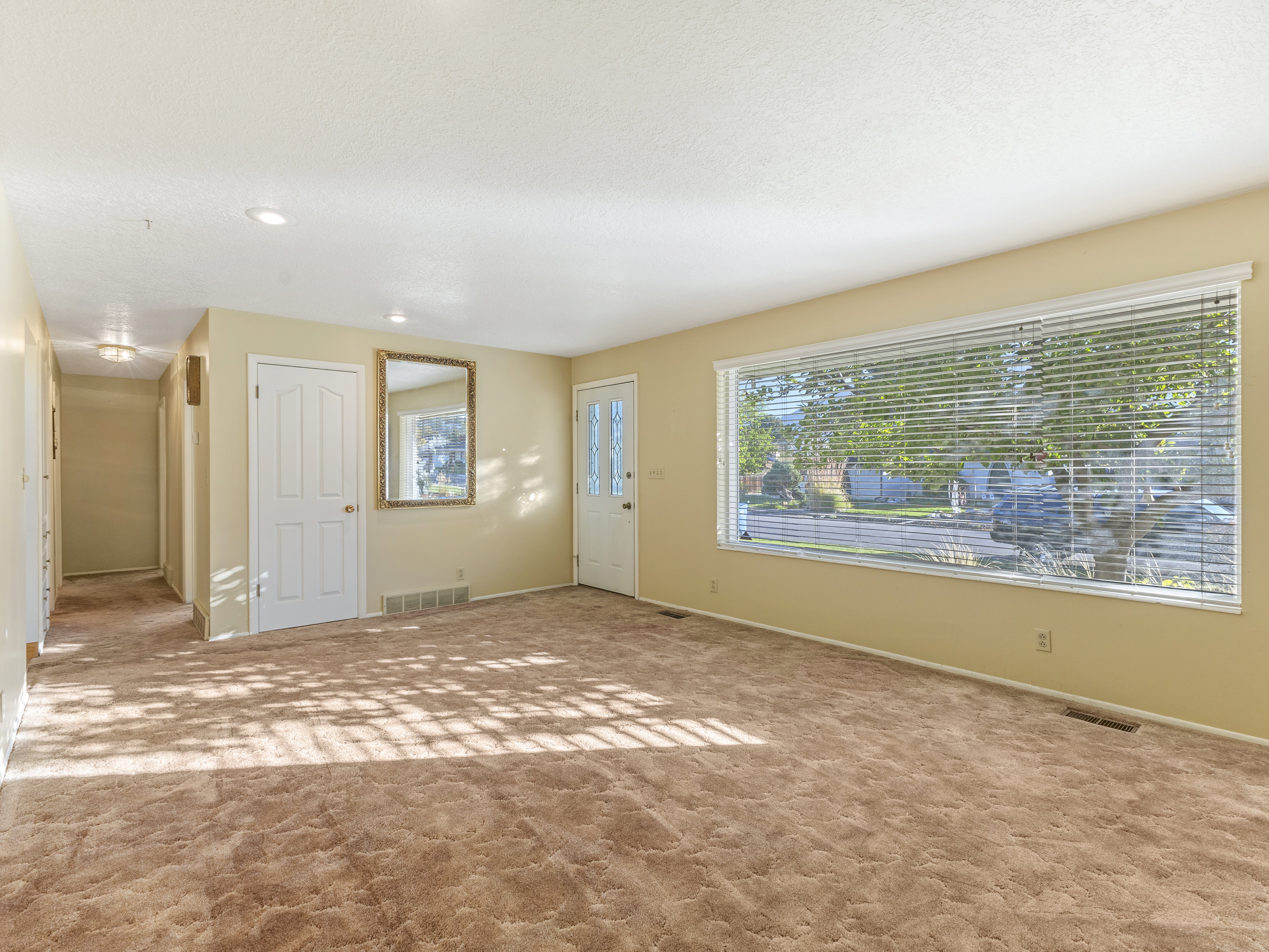 Expansive main living area featuring a large picture window with horizontal blinds, carpet flooring, recessed lighting, and a white paneled door