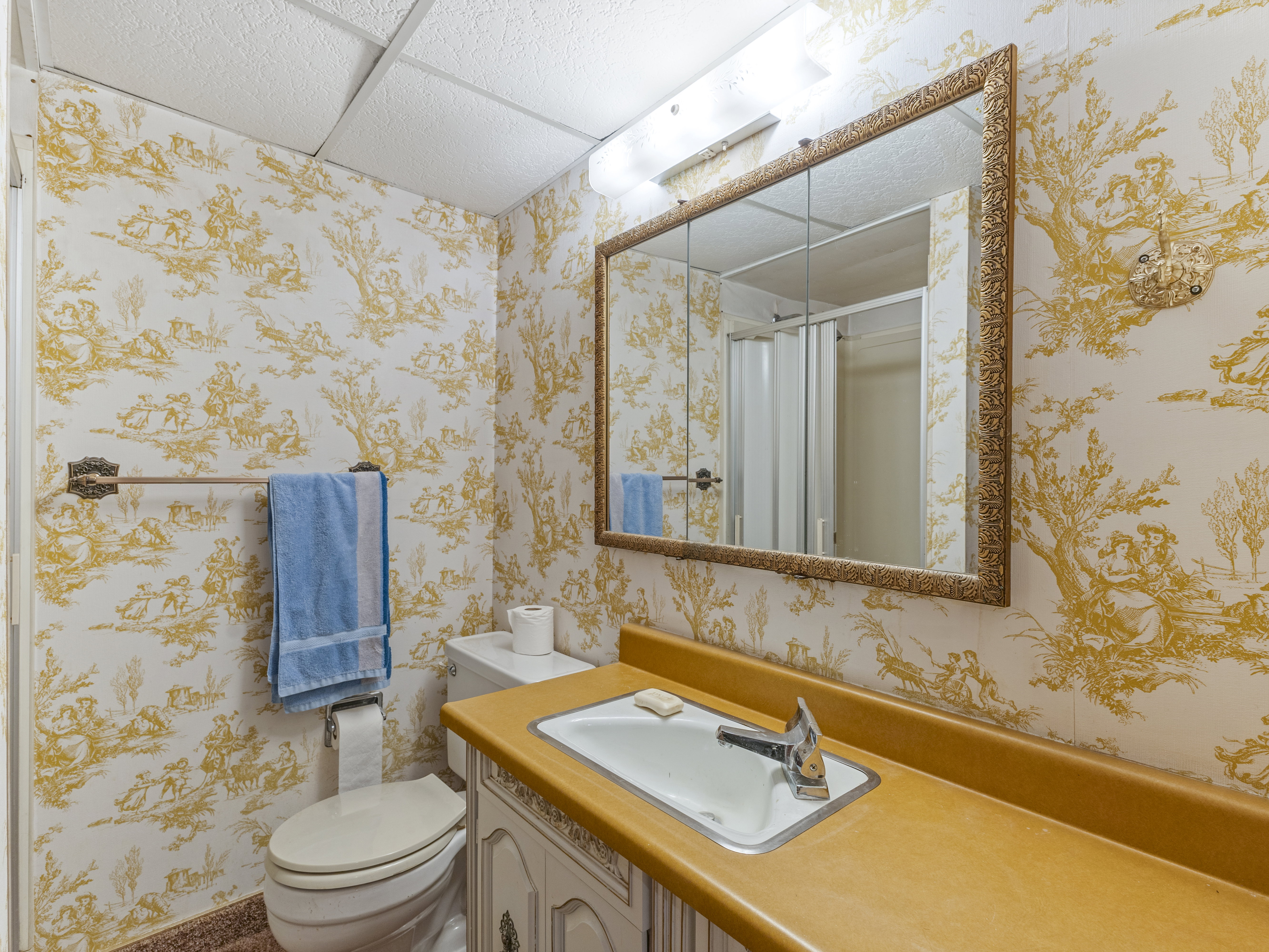 Bathroom featuring patterned wallpaper, a vanity with an integrated sink, a framed medicine cabinet, and a shower enclosure