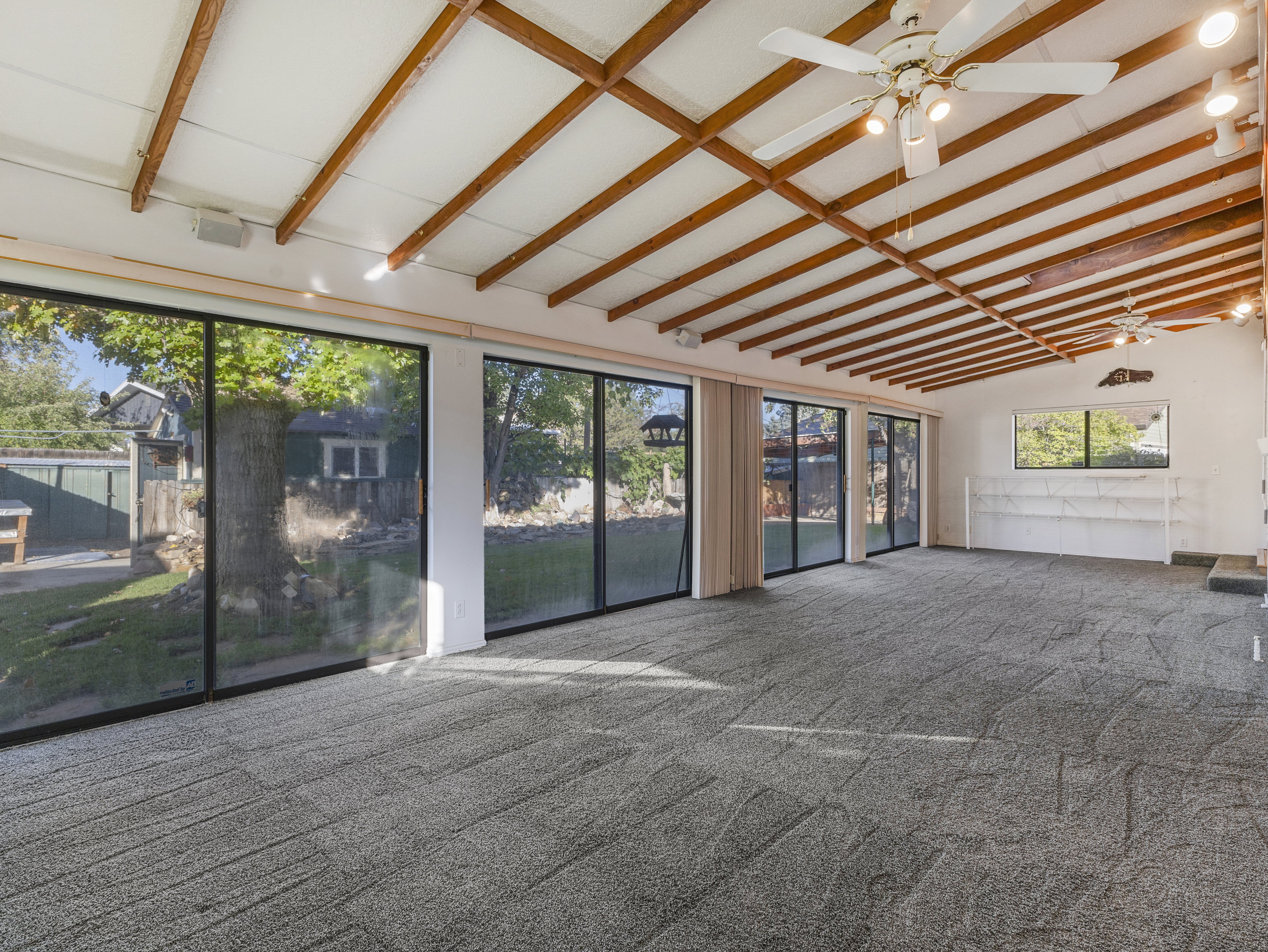 Expansive room featuring a vaulted ceiling with exposed wood beams, multiple ceiling fans, and track lighting