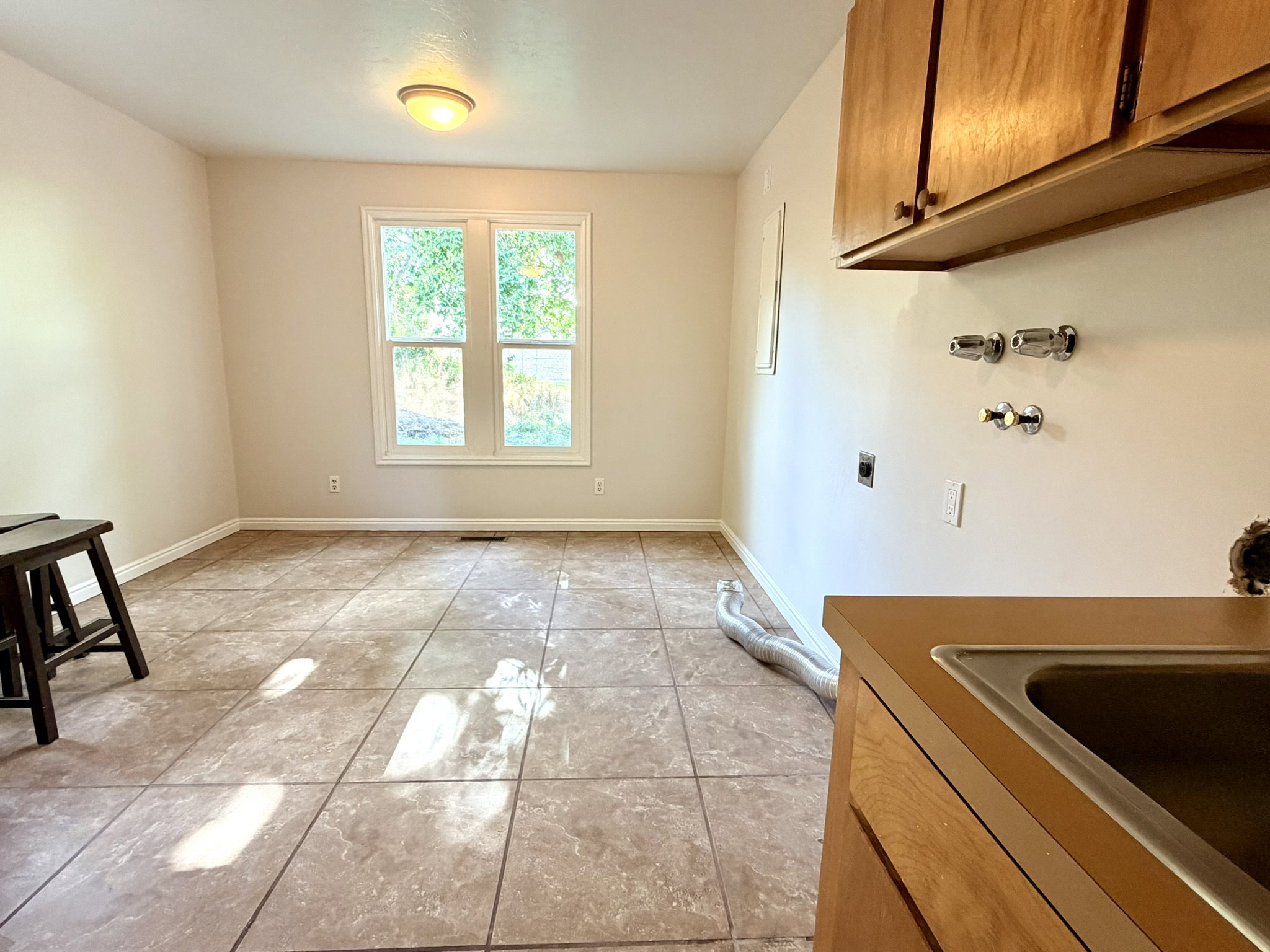 Utility room featuring neutral wall tones, ceramic tile flooring, a double window, and wood cabinetry with a utility sink