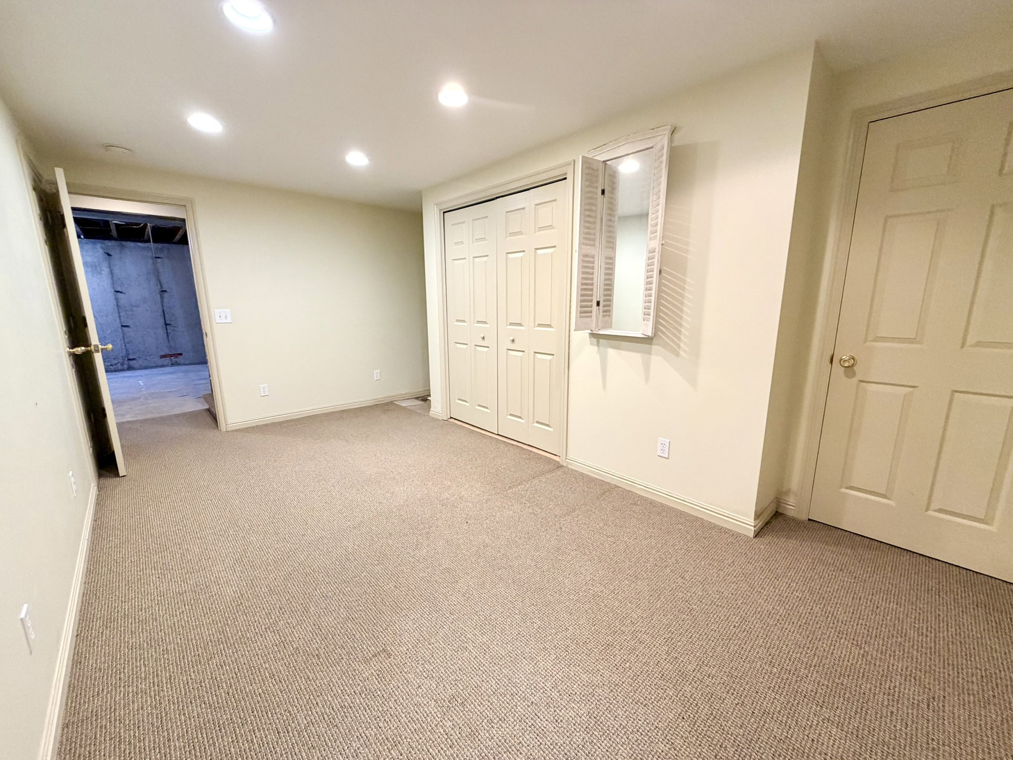 Carpeted room featuring recessed lighting, a bifold door closet, an interior door with brass hardware, and a decorative wall mirror with shutter details