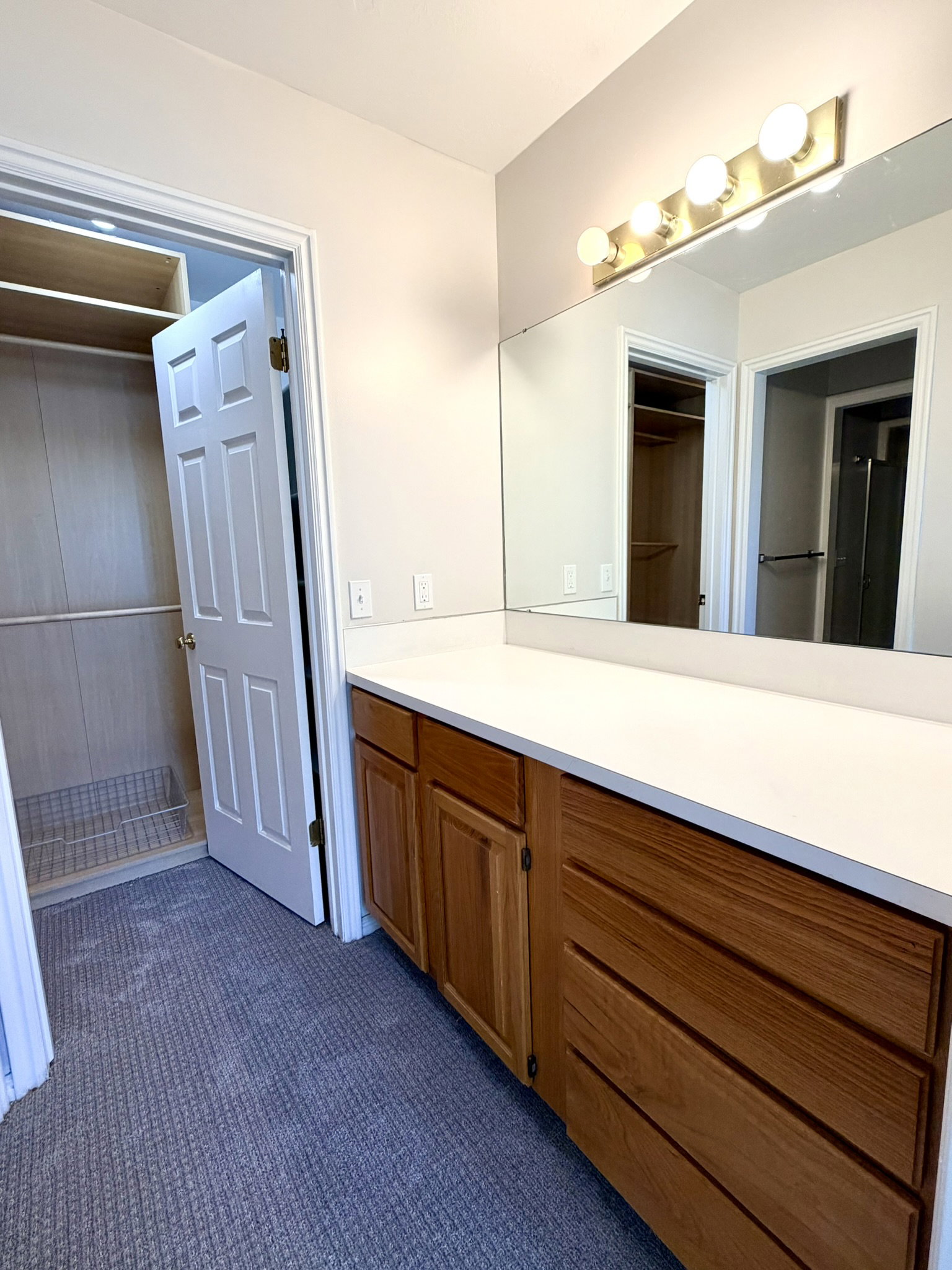 Vanity area featuring a wood-finish cabinet with multiple drawers and doors, a white countertop, and a full-width mirror with a four-bulb vanity light fixture in Primary bathroom