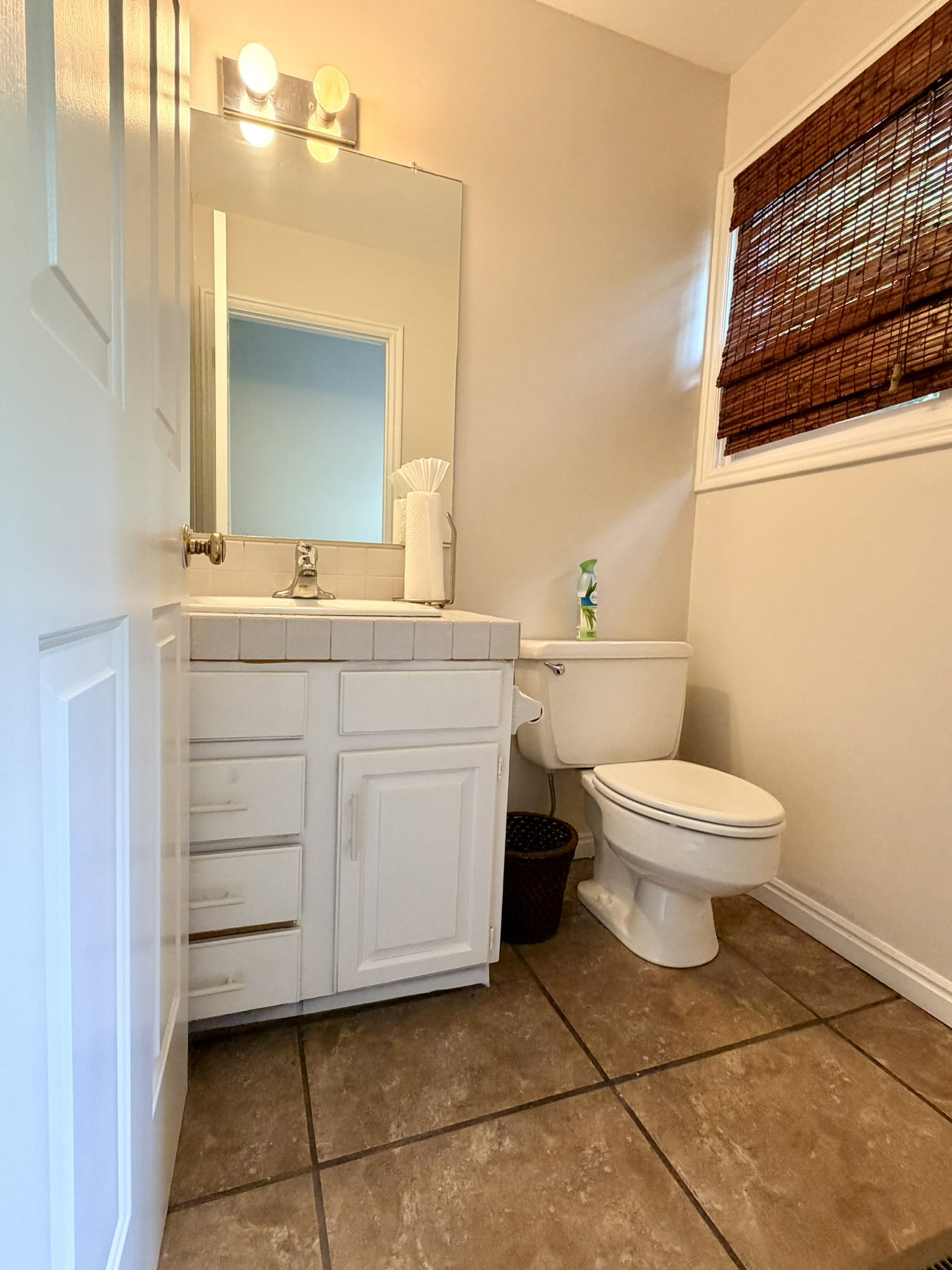 Ceramic tile flooring, white vanity with integrated sink, rectangular mirror, and wall-mounted lighting fixture