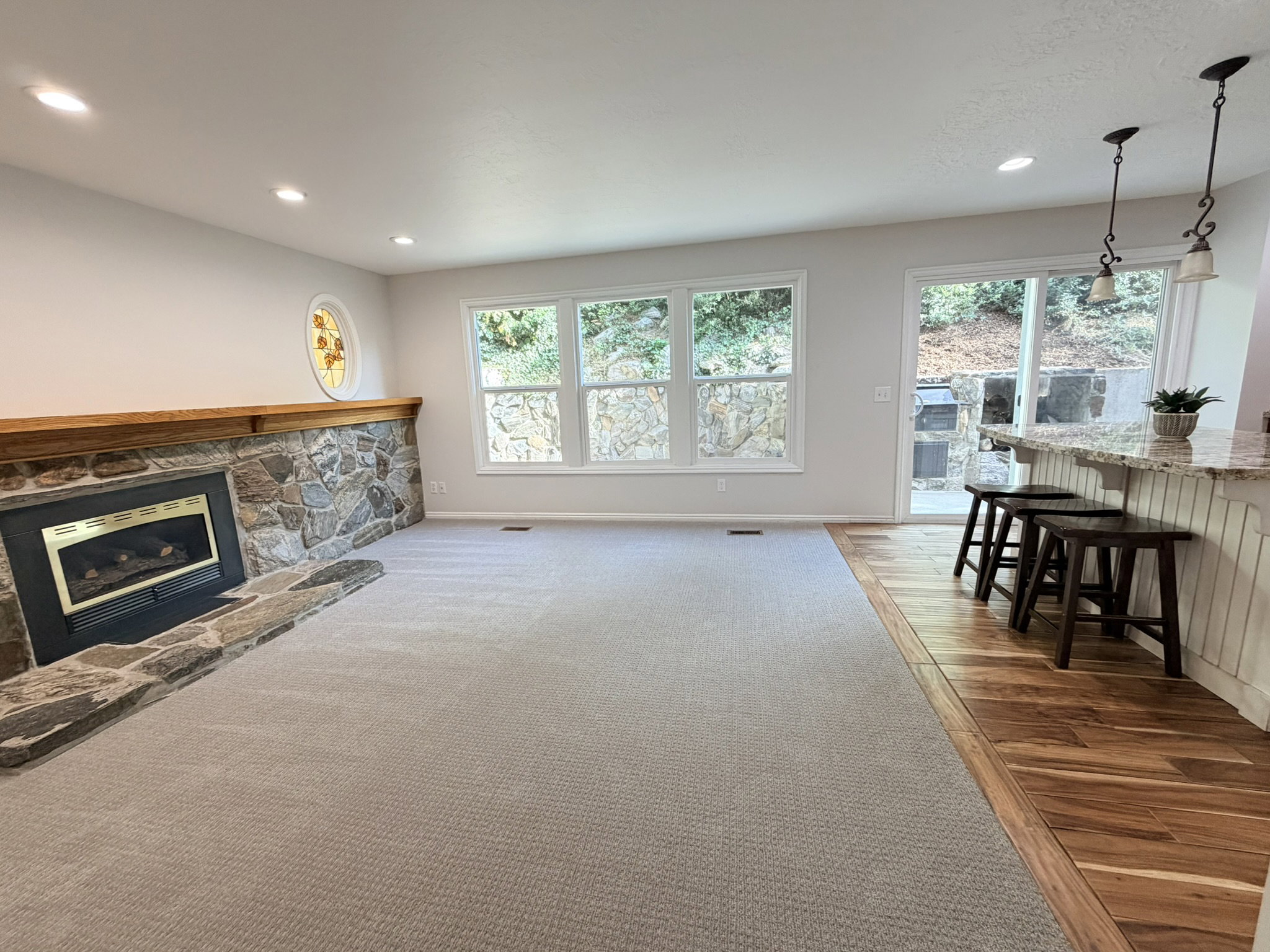 Spacious living area featuring a stone-clad fireplace with a wood mantel, multiple windows, recessed lighting, and a stained glass accent window