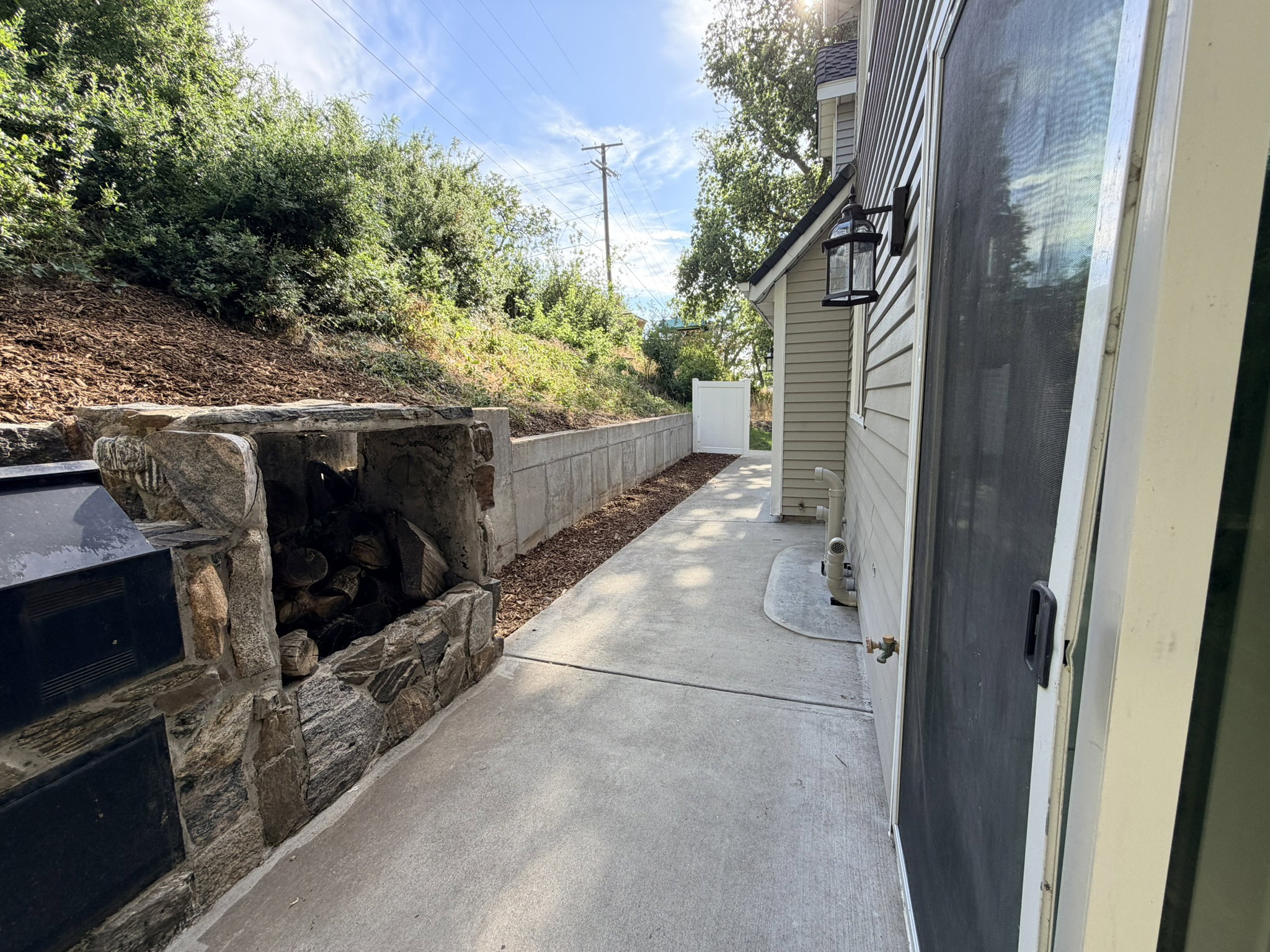 Concrete pathway featuring a stone-clad outdoor fireplace with log storage