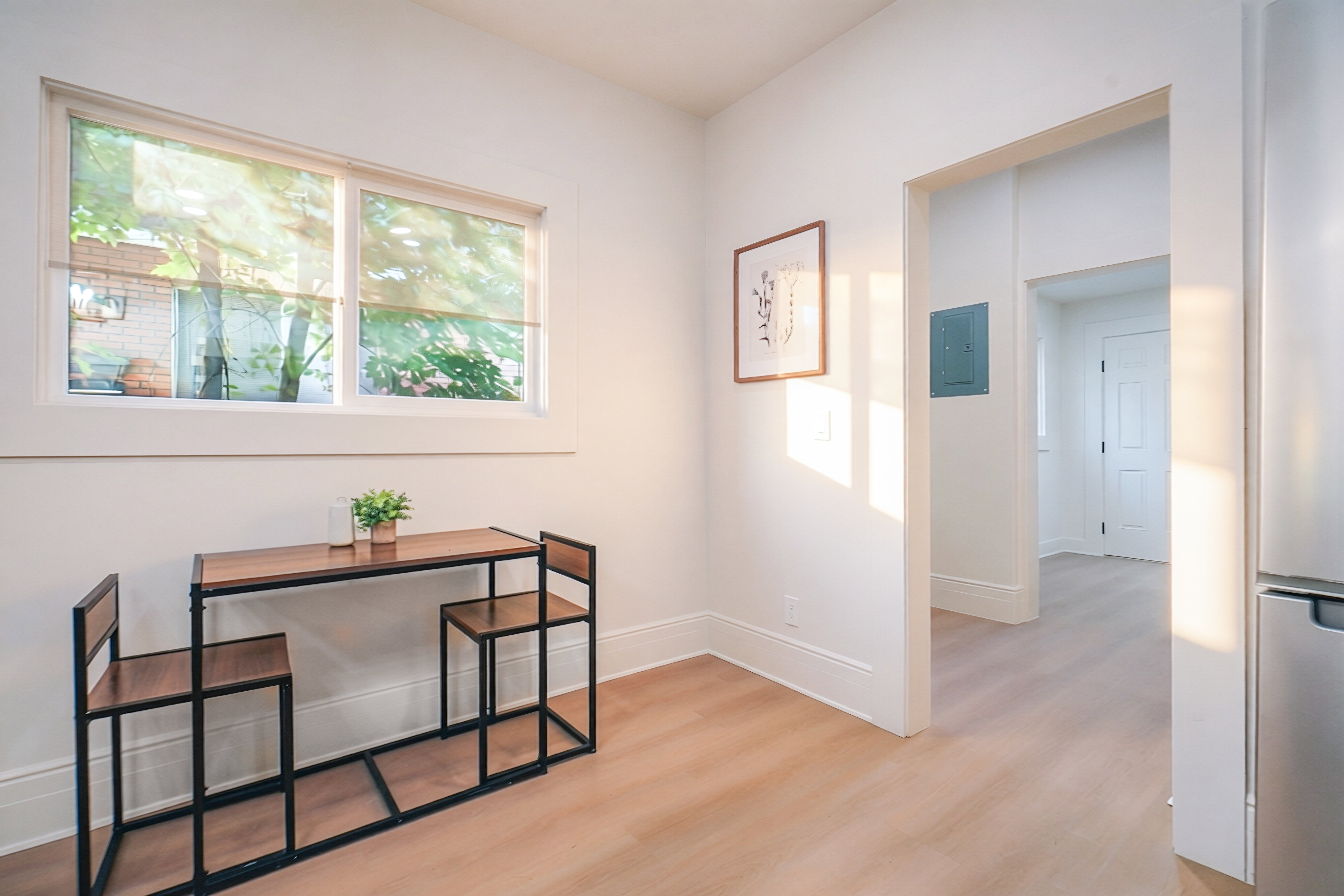 Bright interior space featuring a window with white trim, light wood-finish flooring, and white baseboards