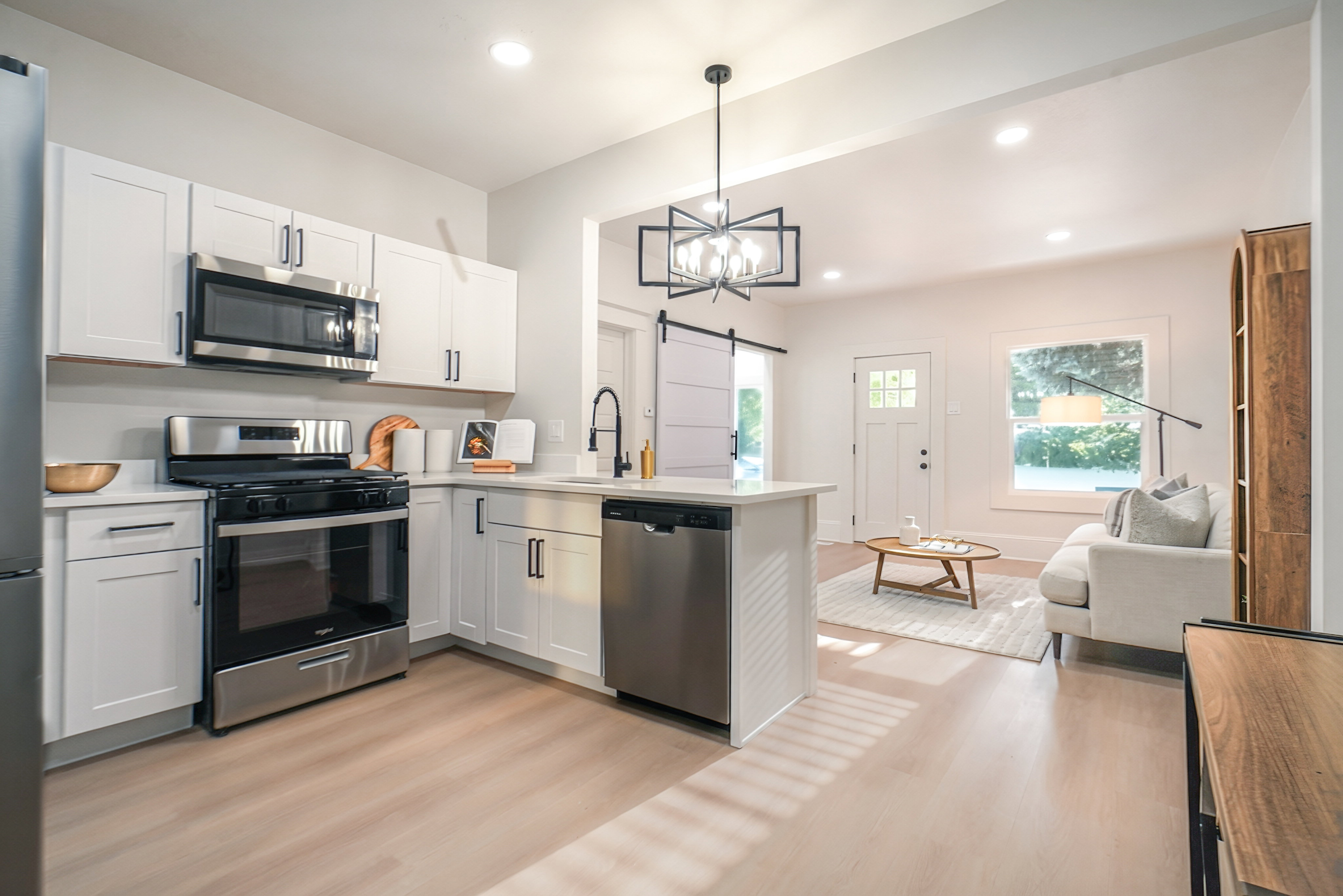 Open-concept kitchen and living area featuring stainless steel appliances, white shaker cabinetry, light wood-finish flooring, recessed lighting, and a modern geometric chandelier