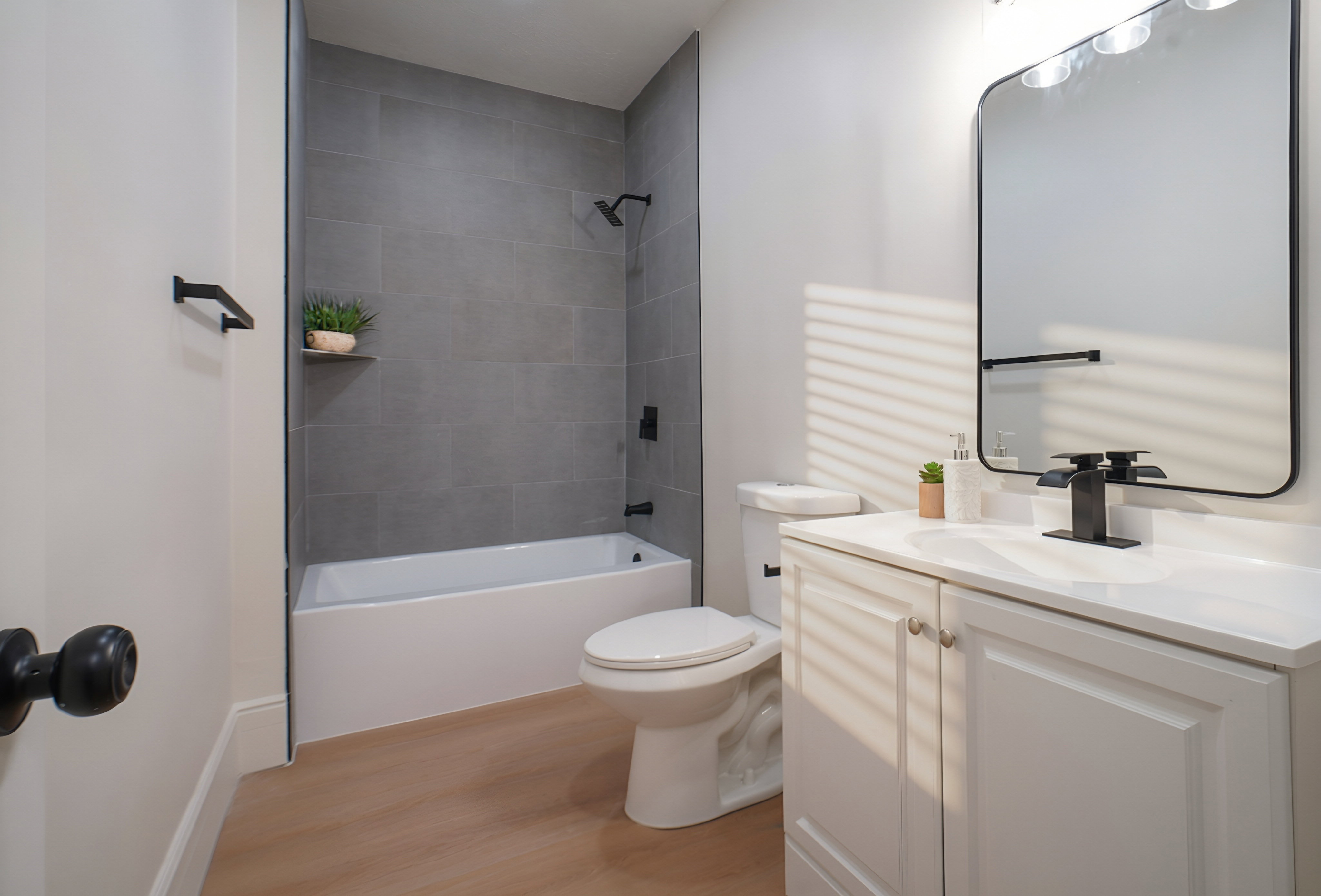 Contemporary bathroom featuring a white vanity with integrated sink, matte black fixtures, a rectangular mirror, a white bathtub, and large format grey wall tiling