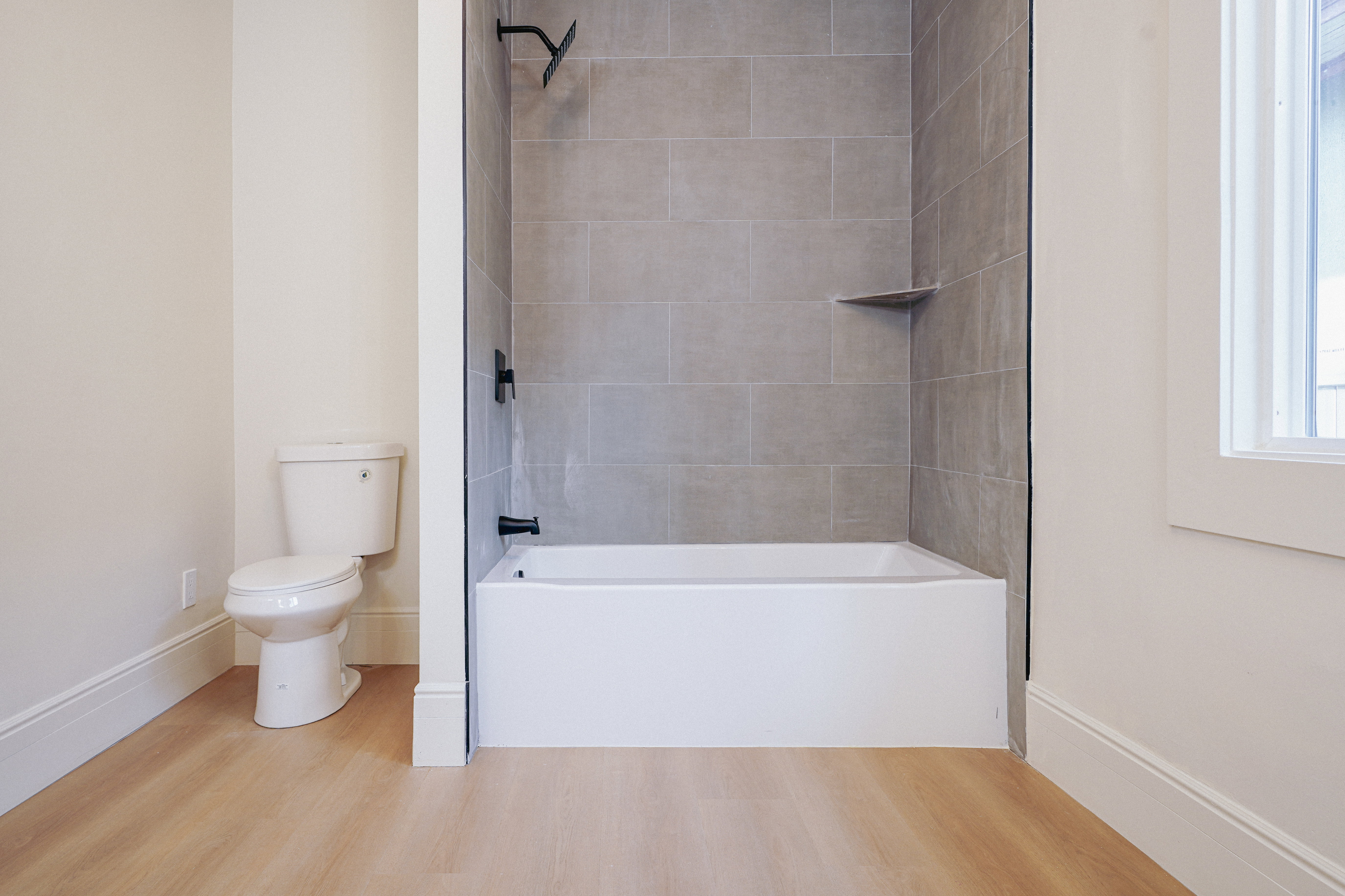 Bathroom featuring a white tub with matte black fixtures, grey rectangular tile surround, and an integrated shower shelf