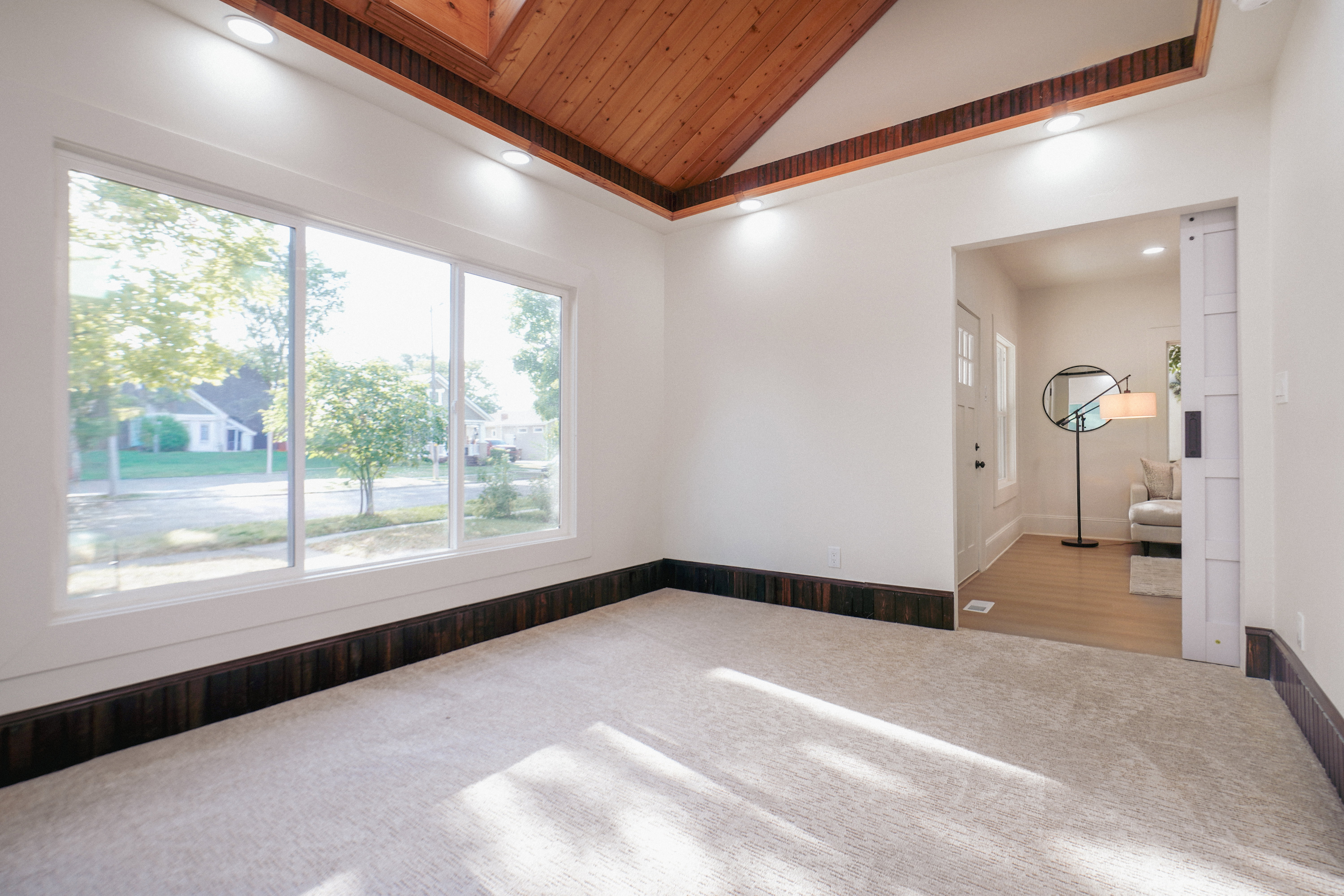 Spacious room featuring a vaulted wood-paneled ceiling, recessed lighting, and a large multi-pane window