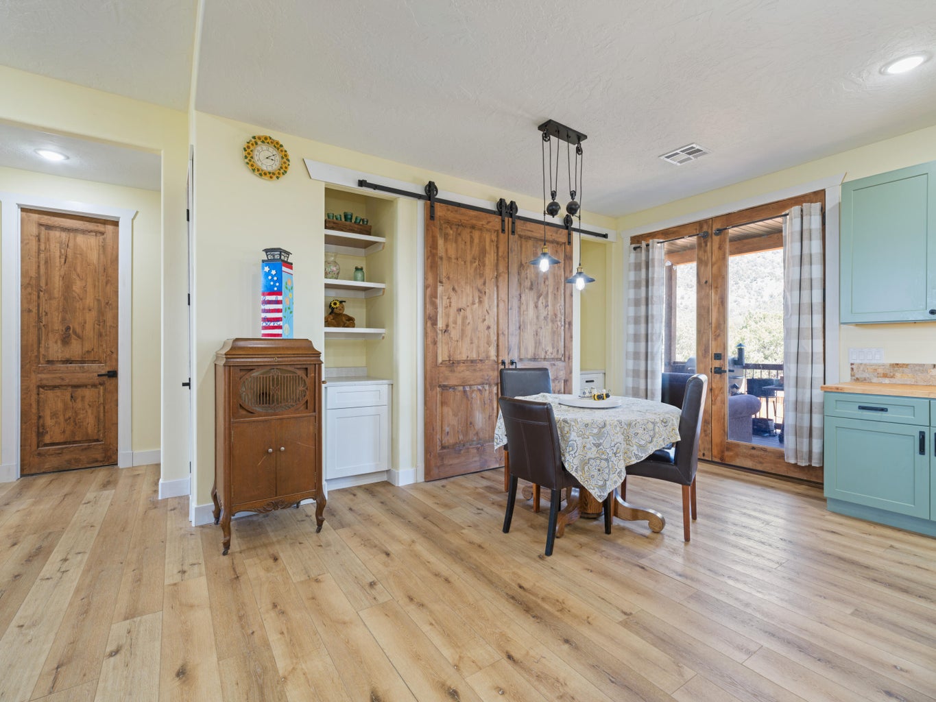 Dining area featuring wood-finish flooring, a contemporary linear chandelier, wooden barn doors, built-in shelving with lower cabinetry, and double French doors opening to an outdoor space