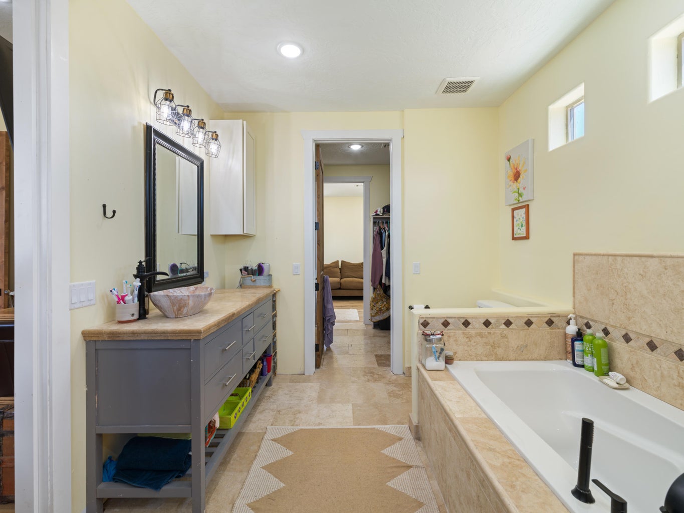 Bathroom featuring a built-in soaking tub, a vanity with stone counter, vessel sink, and an overhead light fixture