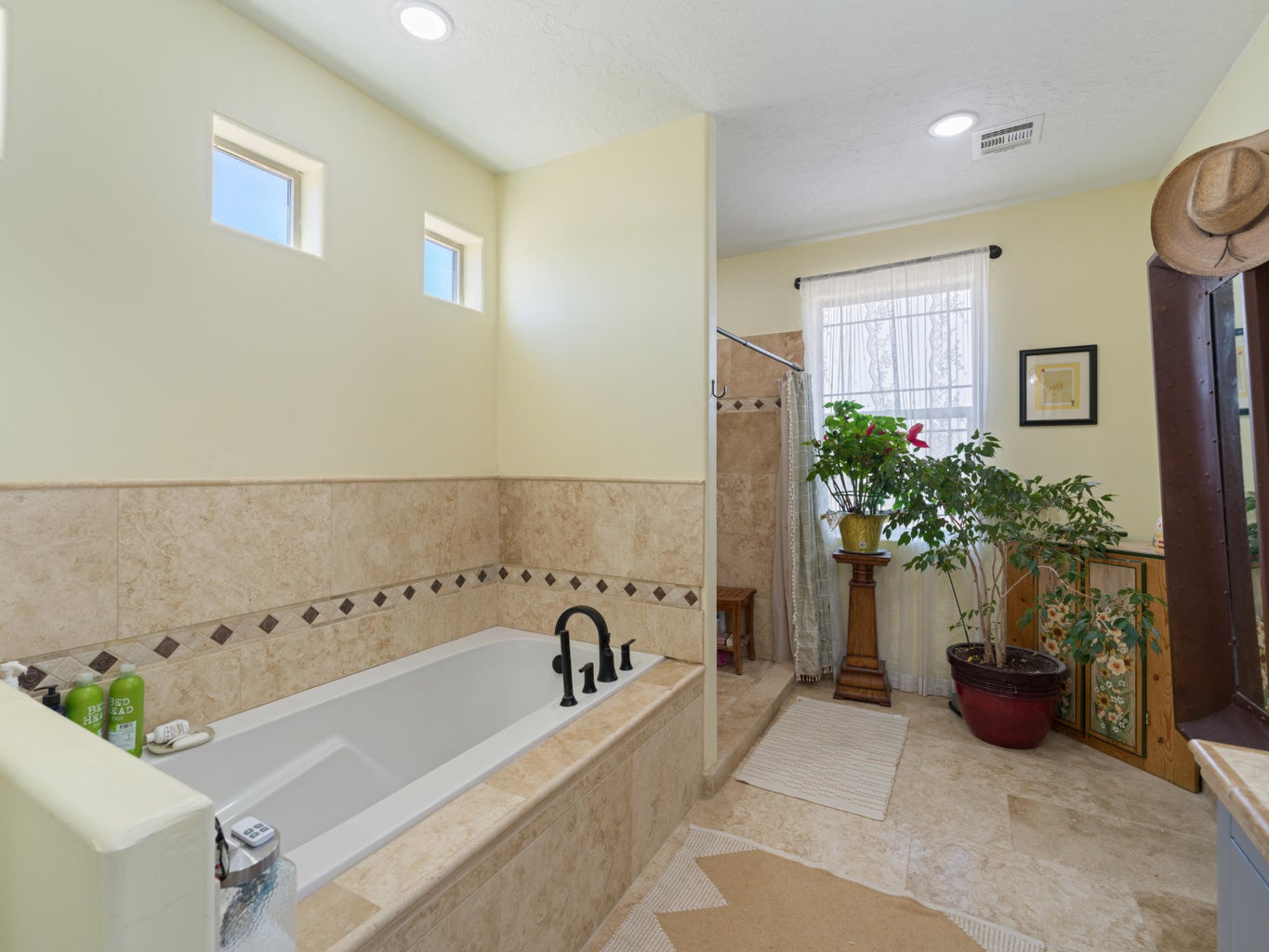 Soaking tub with a black faucet, surrounded by natural stone-look tile with decorative accents