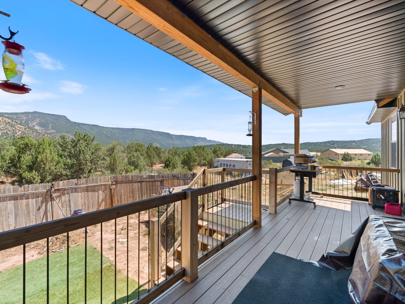 Expansive covered deck featuring wood-finish composite decking, wooden railings with black metal balusters, and a solid roof
