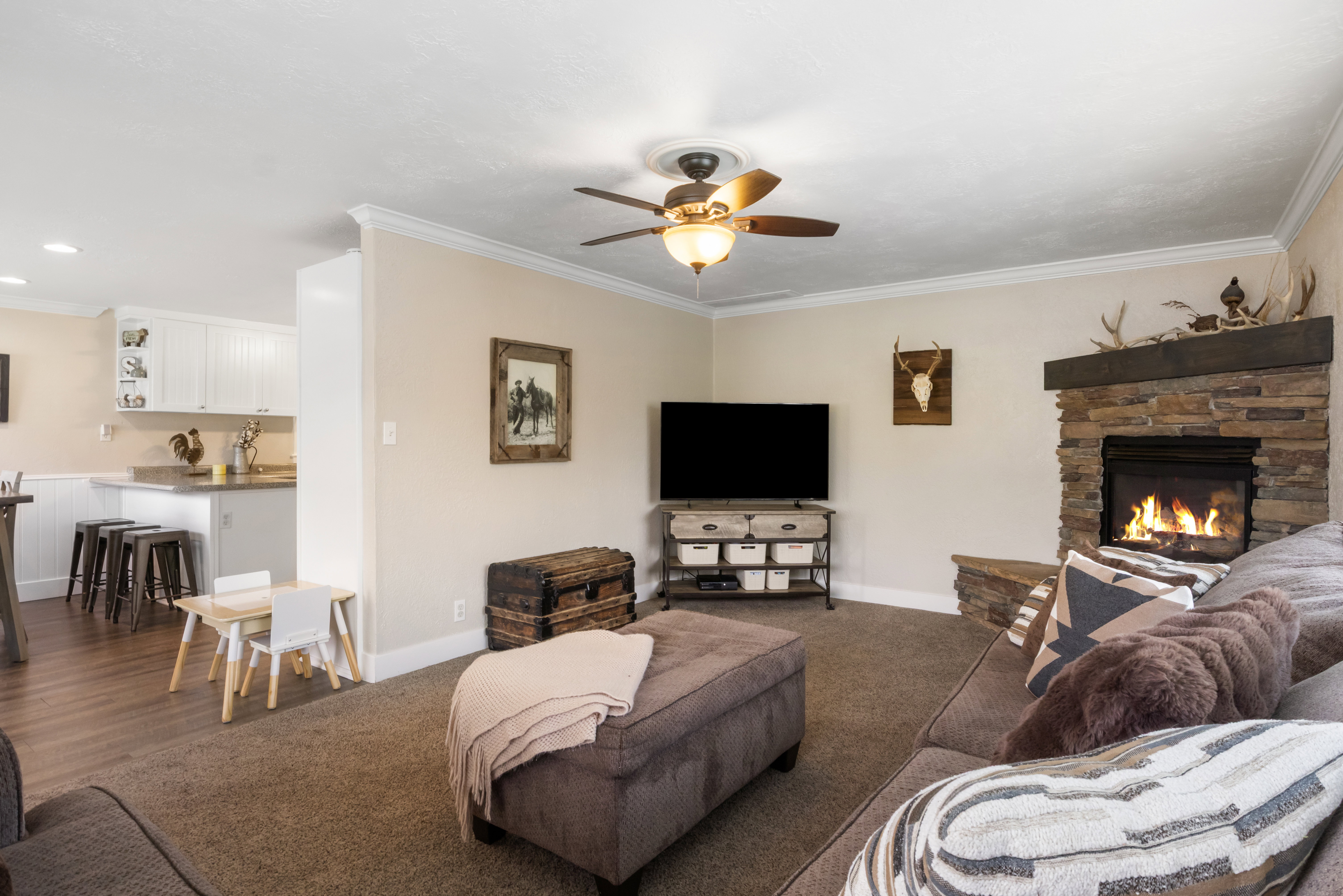 Living space featuring a stone-clad fireplace with a wood mantel, crown molding, and a ceiling fan