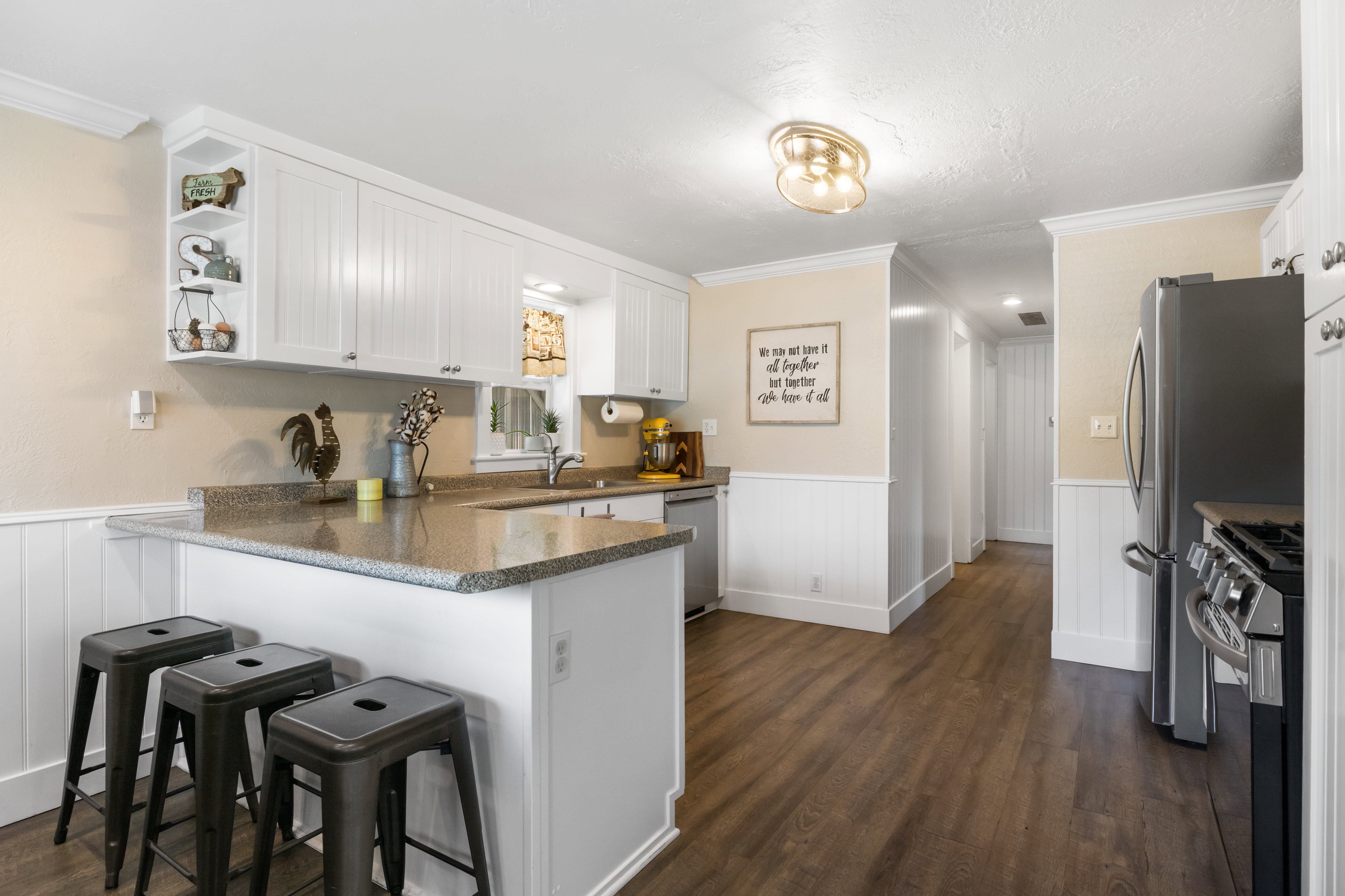 Kitchen featuring white cabinetry, a peninsula with a stone-finish countertop, stainless steel appliances, and wood-finish flooring
