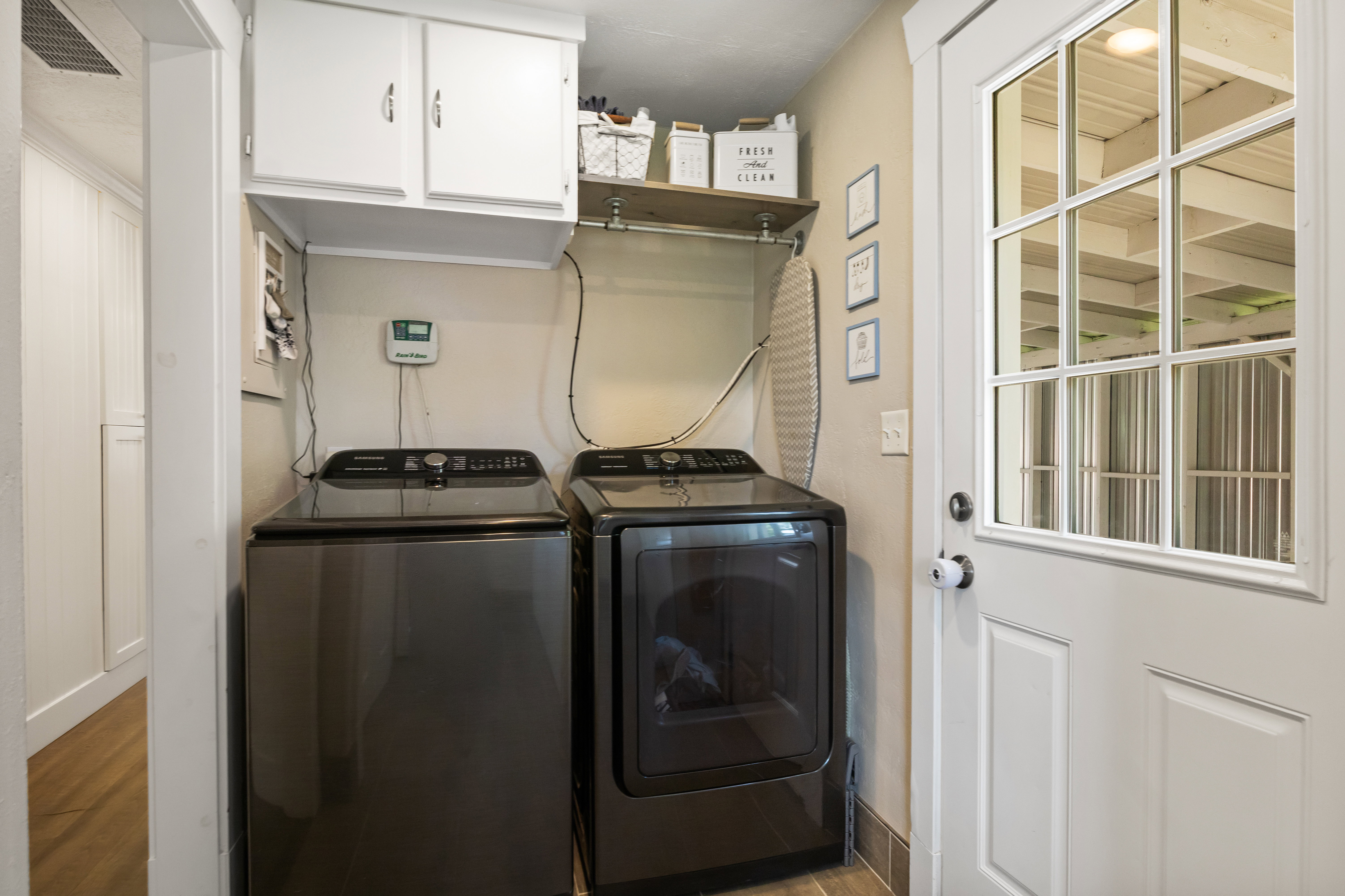 Dedicated laundry area featuring overhead cabinetry, wall-mounted shelving, and a paneled glass-insert door