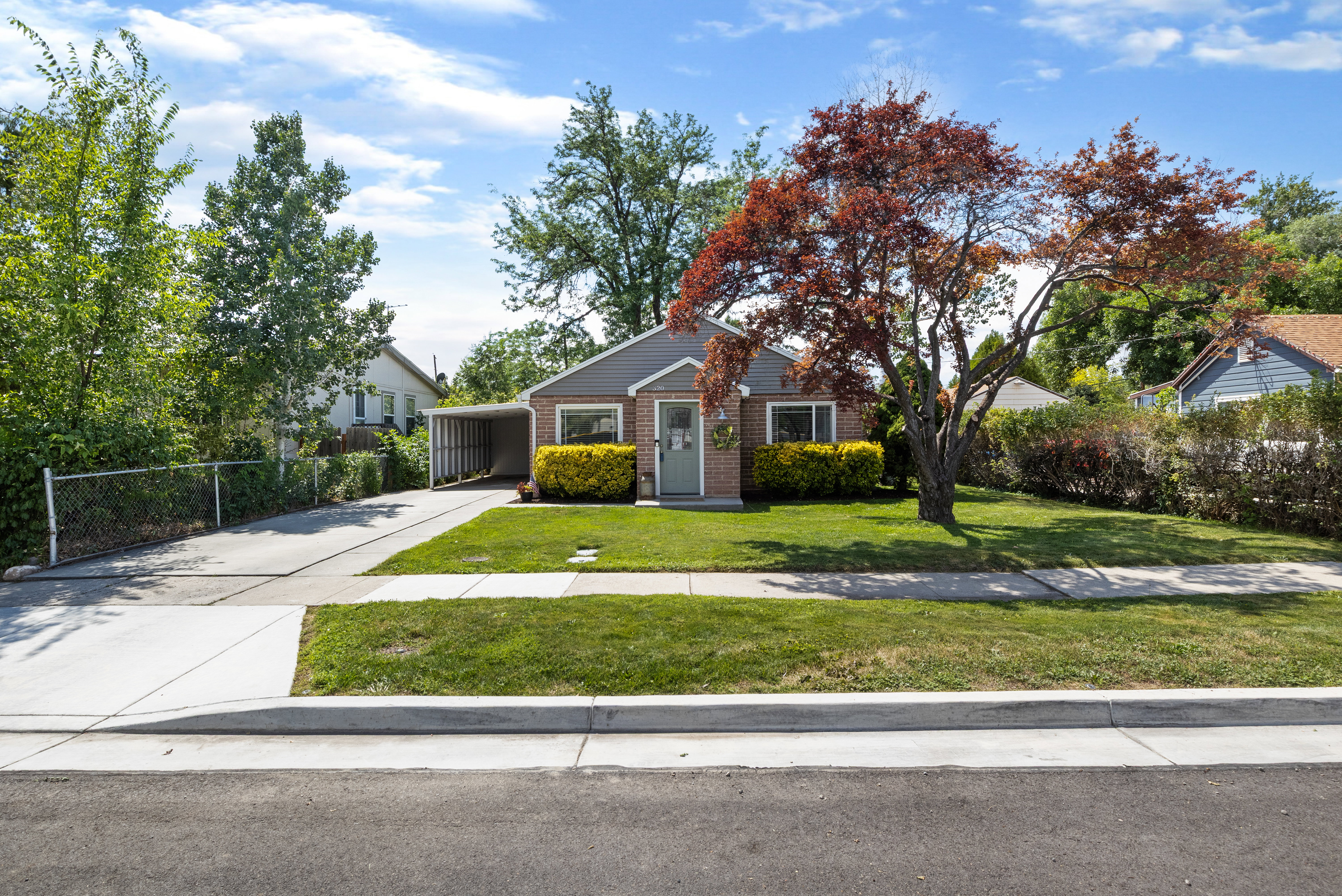 Brick exterior residence with a covered carport, mature trees, a manicured lawn, and a concrete driveway