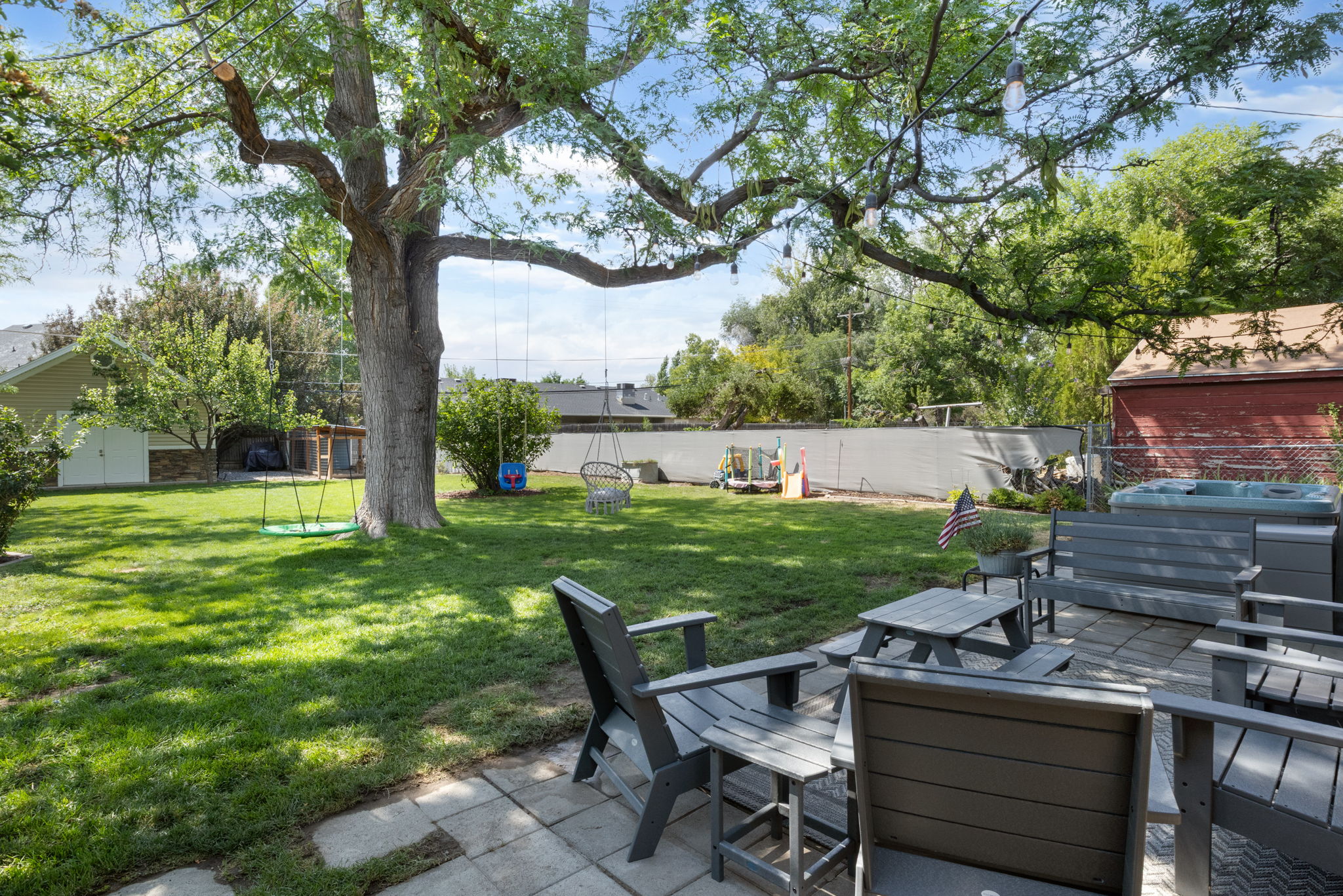 Spacious backyard featuring a large mature tree, a stone paver patio, and a hot tub