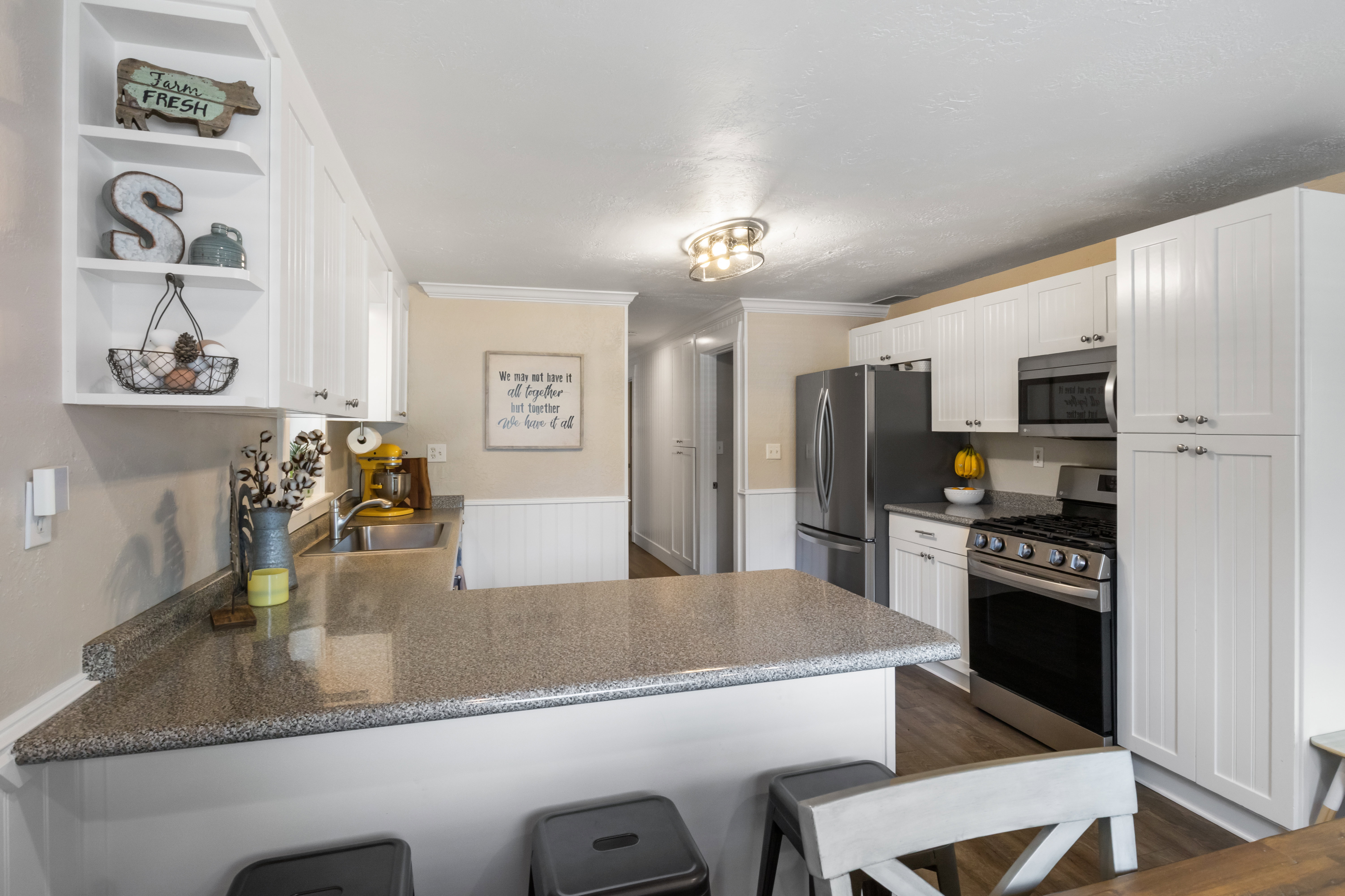 Kitchen featuring white shaker-style cabinetry, a built-in breakfast bar with a speckled countertop, stainless steel appliances, and wood-finish flooring