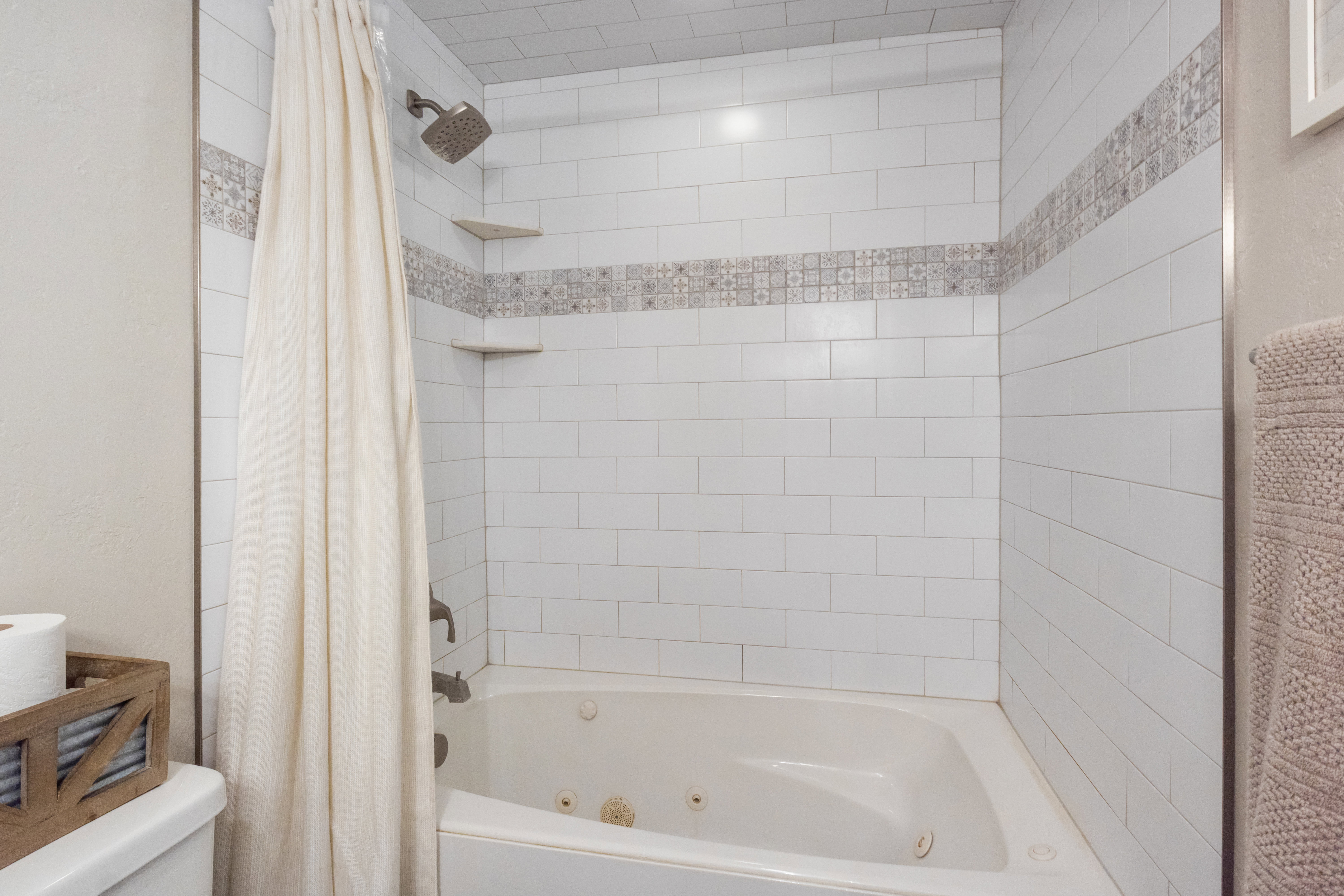 Bathtub with integrated jets, subway tile surround, decorative tile accent band, corner shelving, and a rain showerhead