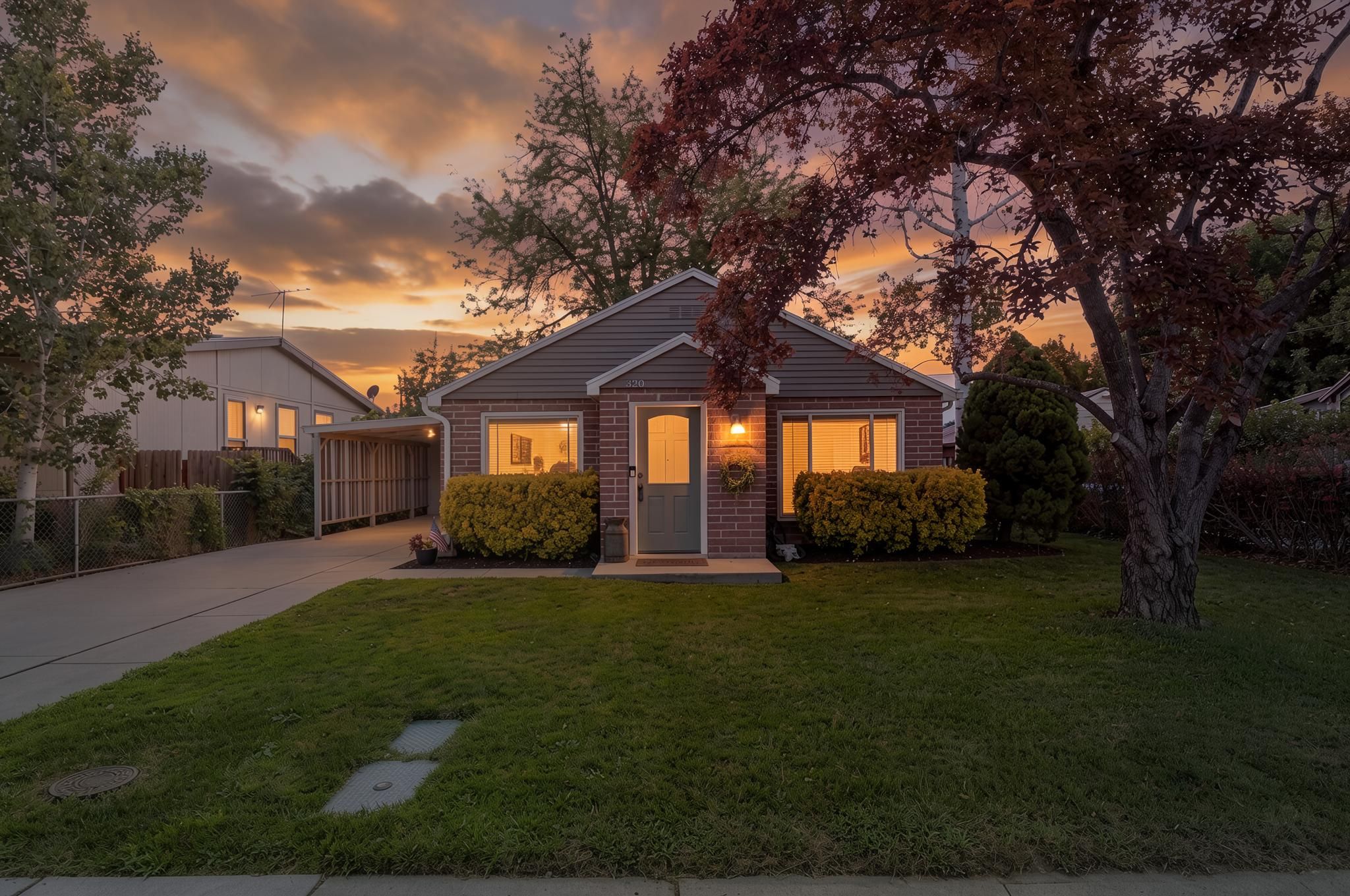 Brick facade home featuring a front lawn, mature trees, a paved driveway, and a covered carport structure