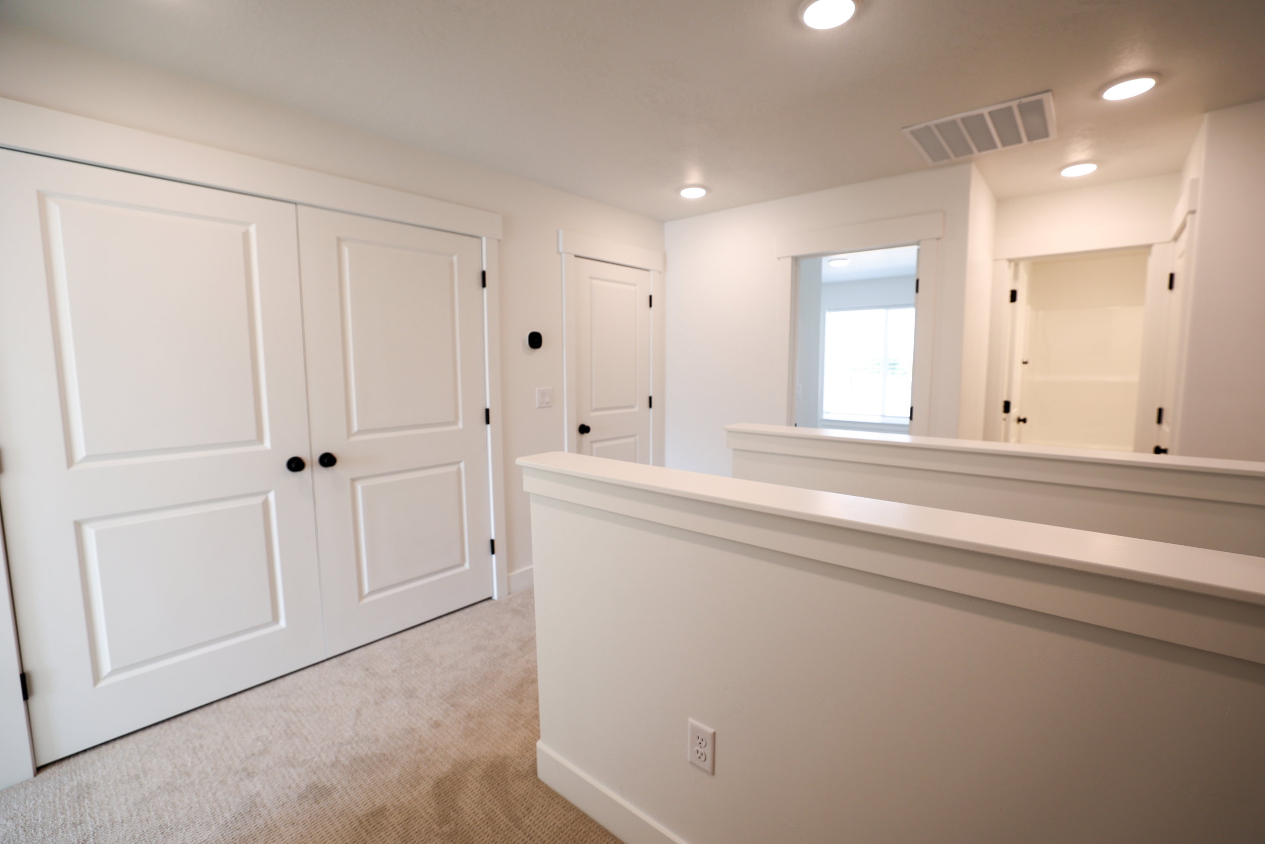 Upper-level landing featuring light-toned carpeting, recessed lighting, and white paneled doors with matte black hardware