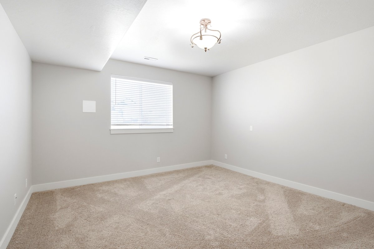 Carpeted room featuring a single window with blinds, a ceiling-mounted light fixture, and white baseboards