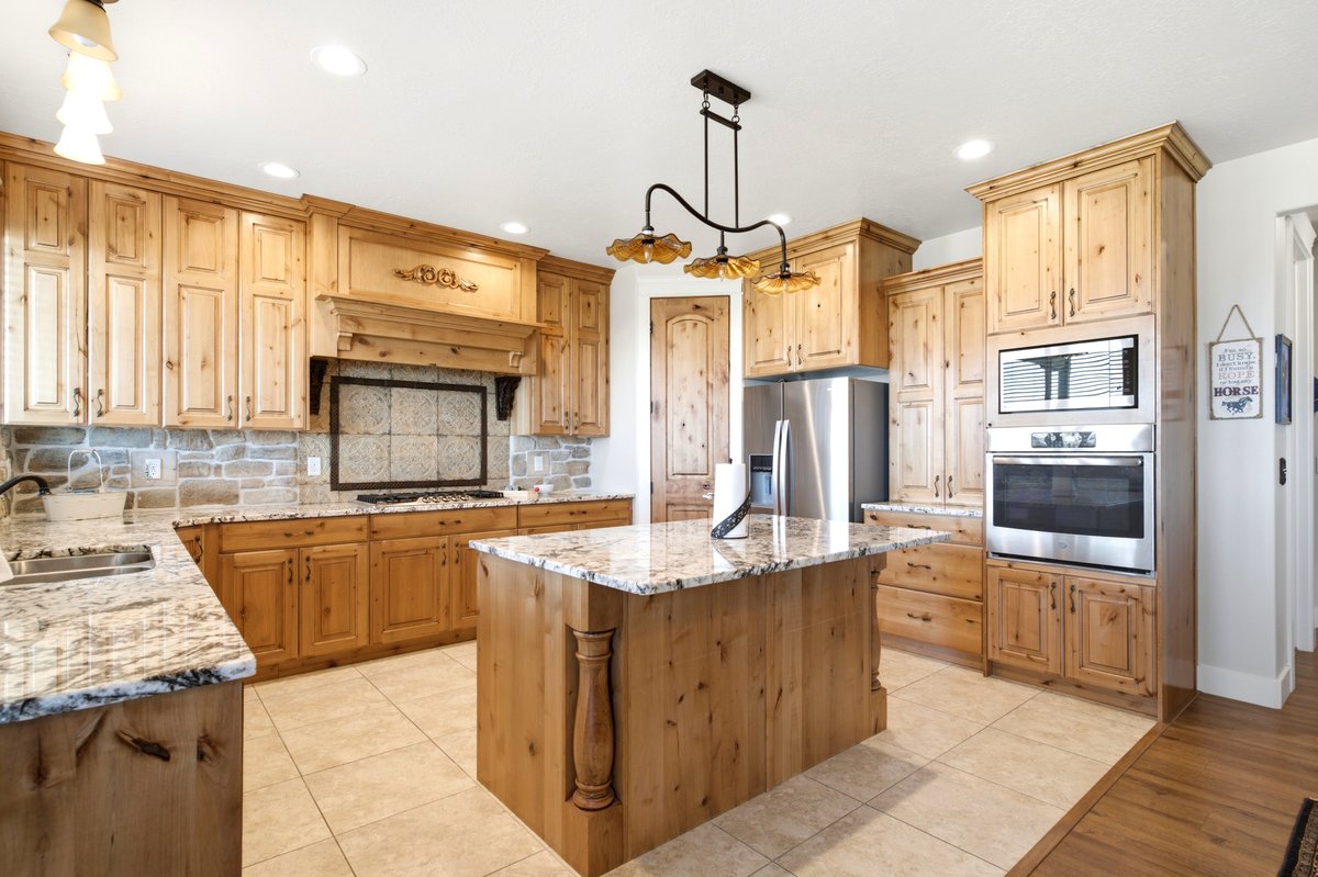 Spacious kitchen featuring extensive light wood cabinetry, stone tile backsplash, granite countertops, and a central island