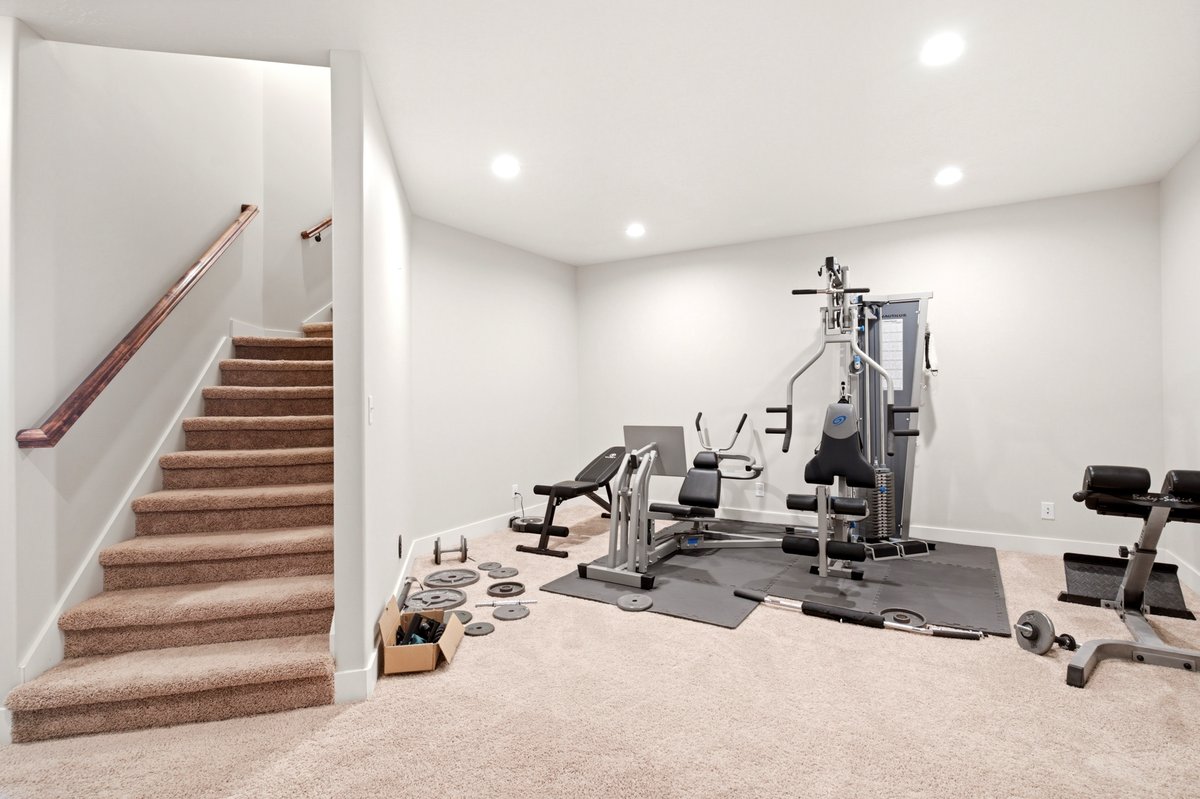 Carpeted staircase with wooden handrail opening to a spacious room featuring recessed lighting and neutral wall tones