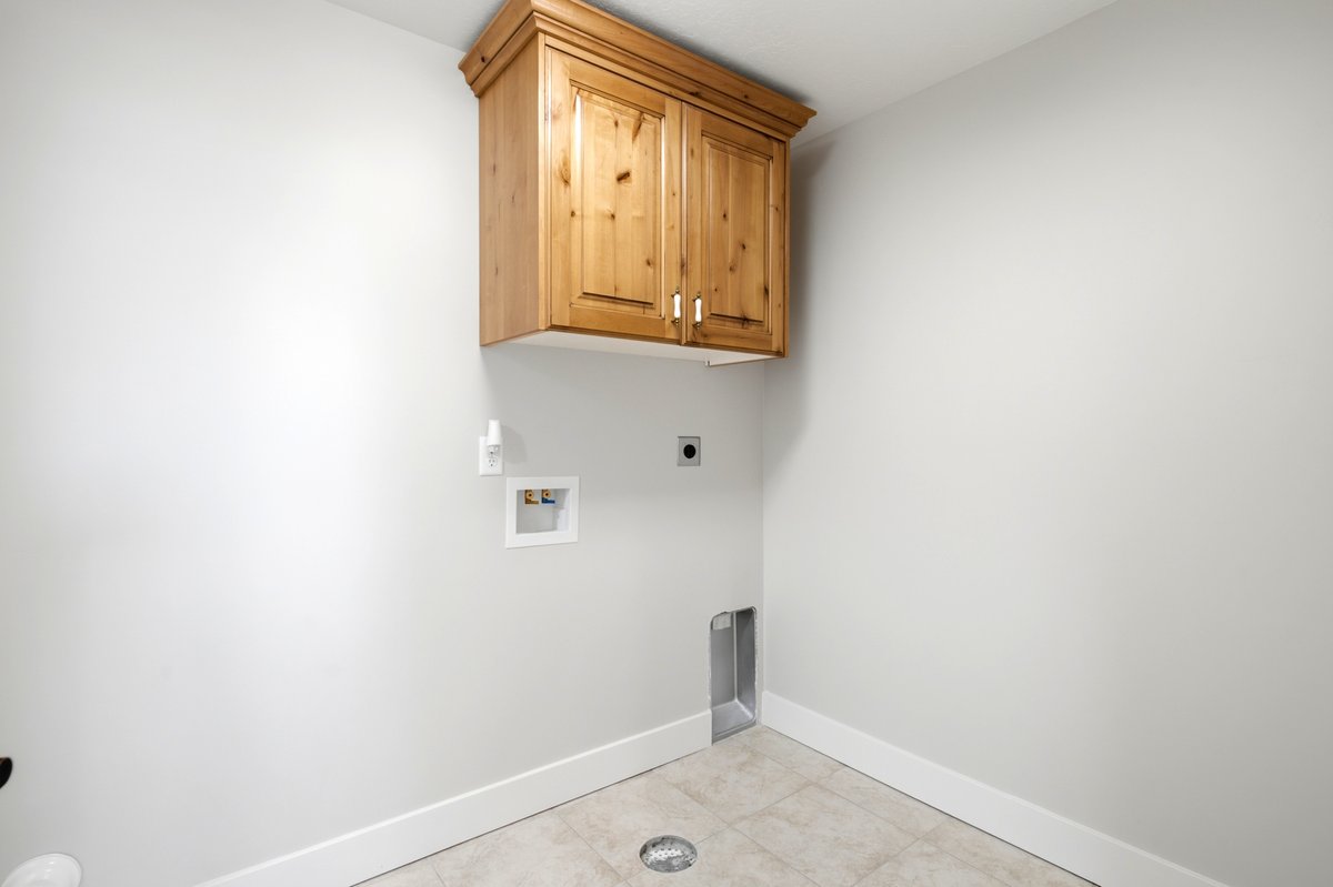Dedicated laundry space featuring a wood-finish wall cabinet with crown molding, tile flooring, and integrated utility connections