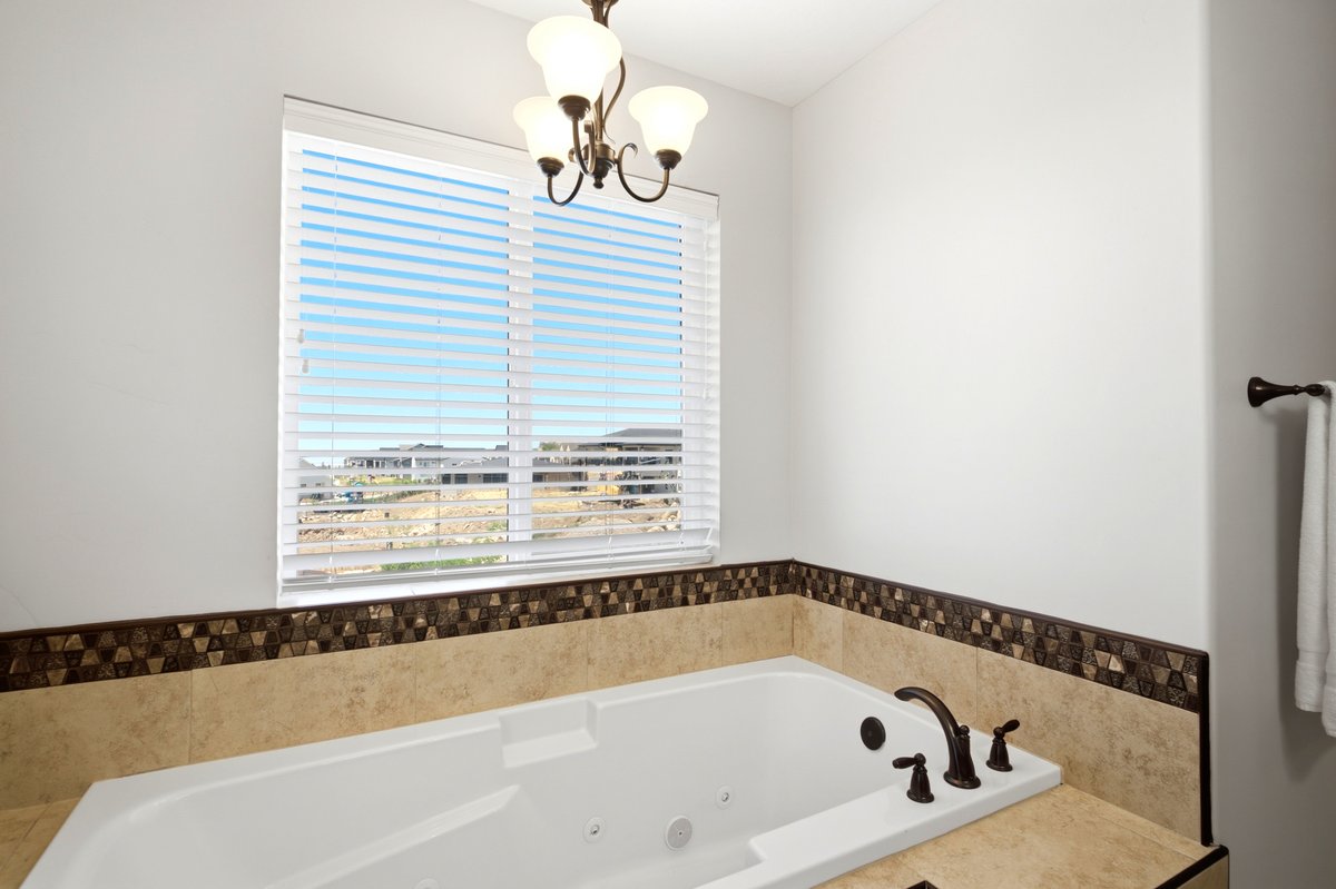 Built-in jetted tub with a bronze-finish faucet, surrounded by a tiled deck and decorative mosaic tile accent