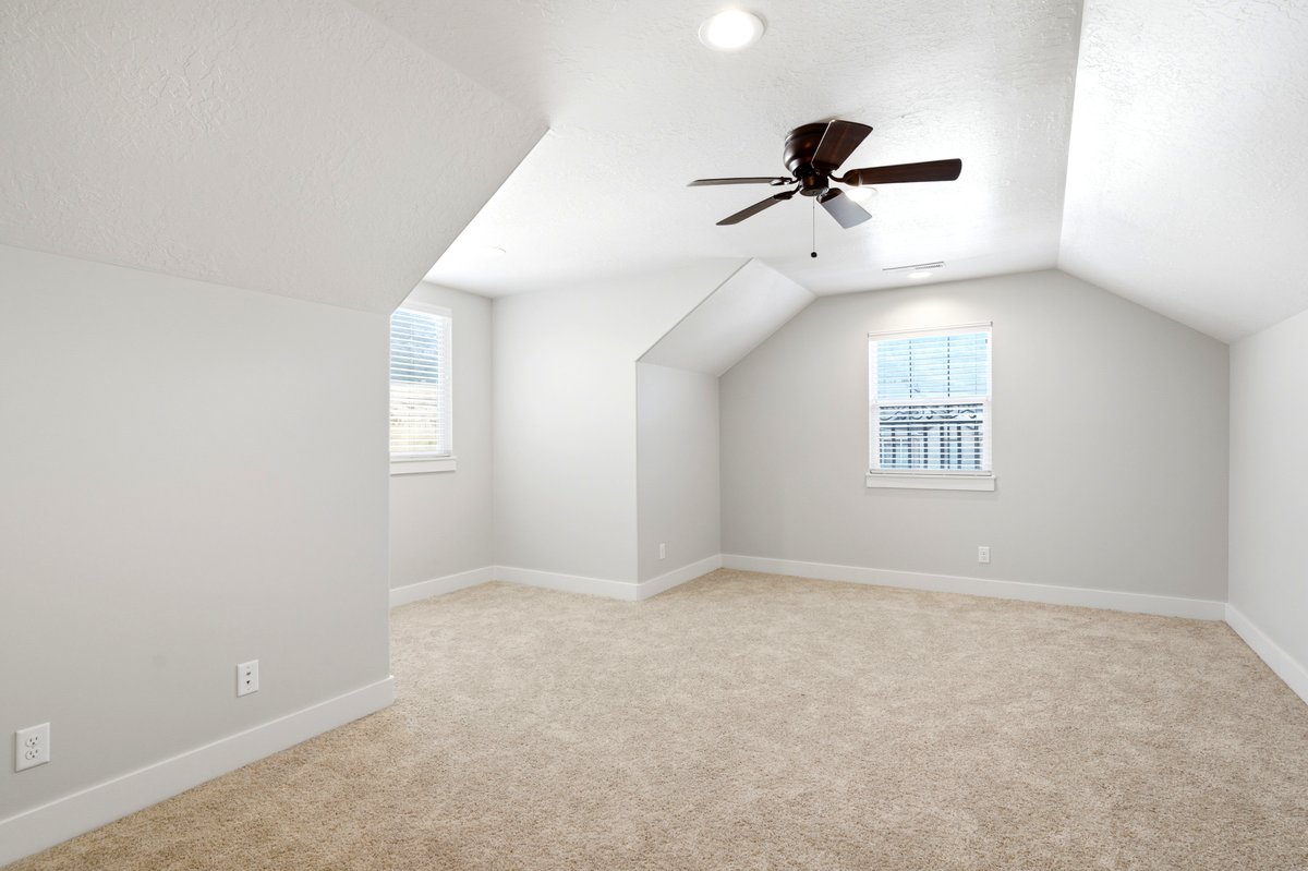 Spacious room featuring vaulted ceilings, neutral-toned carpeting, two windows with blinds, a ceiling fan with integrated lighting, and recessed ceiling lights