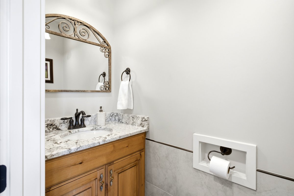 Bathroom featuring a wood vanity with a stone countertop, an undermount sink, and an arched decorative mirror