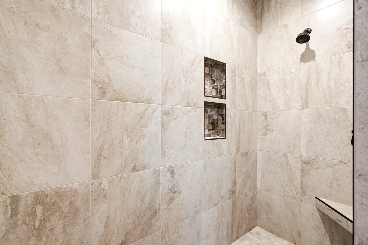 Walk-in shower with large-format beige tiles, two recessed mosaic tile niches, and a corner bench