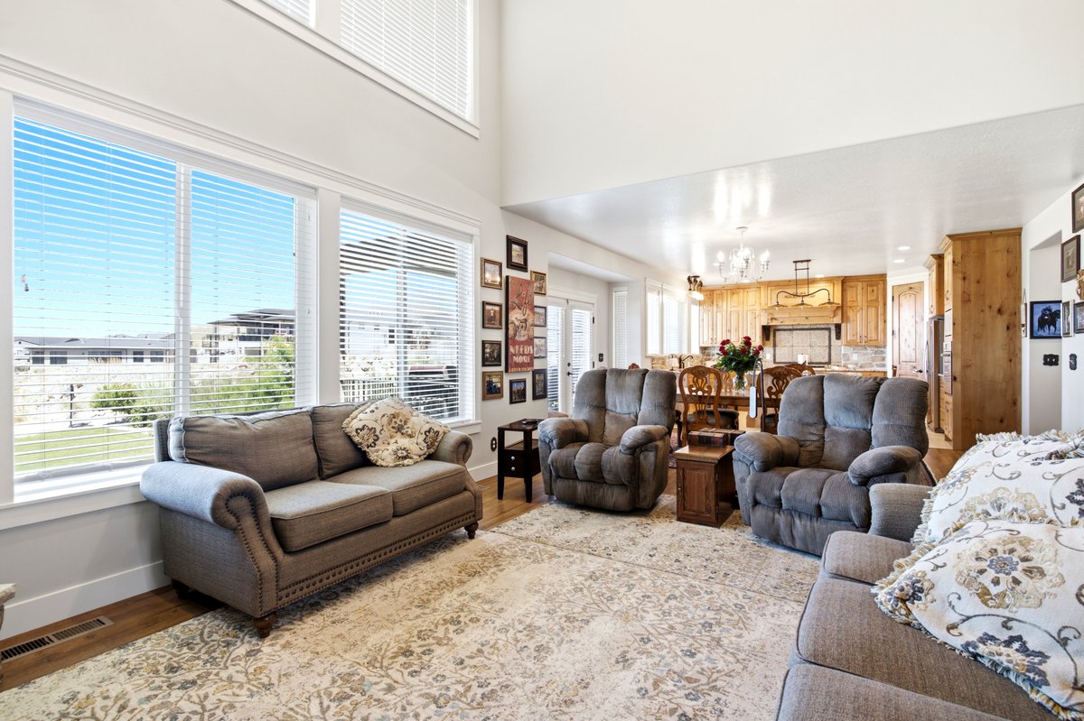 Spacious living area featuring a two-story ceiling, multiple large windows, wood-finish flooring, and an open concept layout connecting to the kitchen and dining area