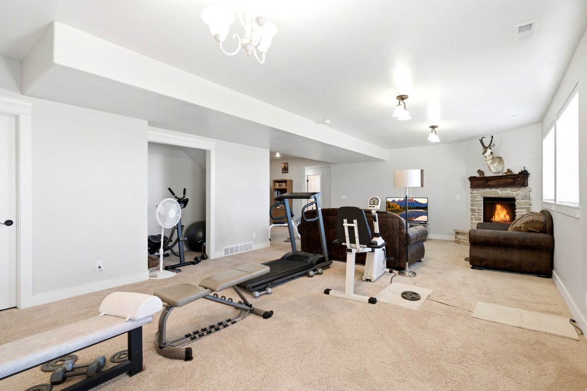 Spacious recreational room featuring a stone-clad fireplace with a decorative mantel, multiple windows for natural light, recessed lighting, and a white ceiling fan light fixture