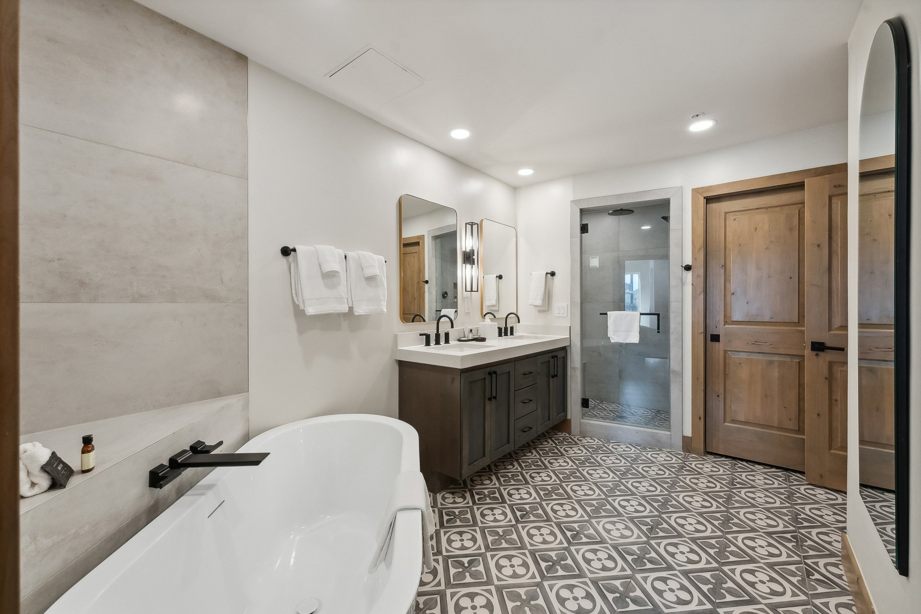 Spacious bathroom featuring a freestanding tub with a matte black faucet, a large walk-in shower with a glass enclosure, a double vanity with ample storage, and patterned floor tiling