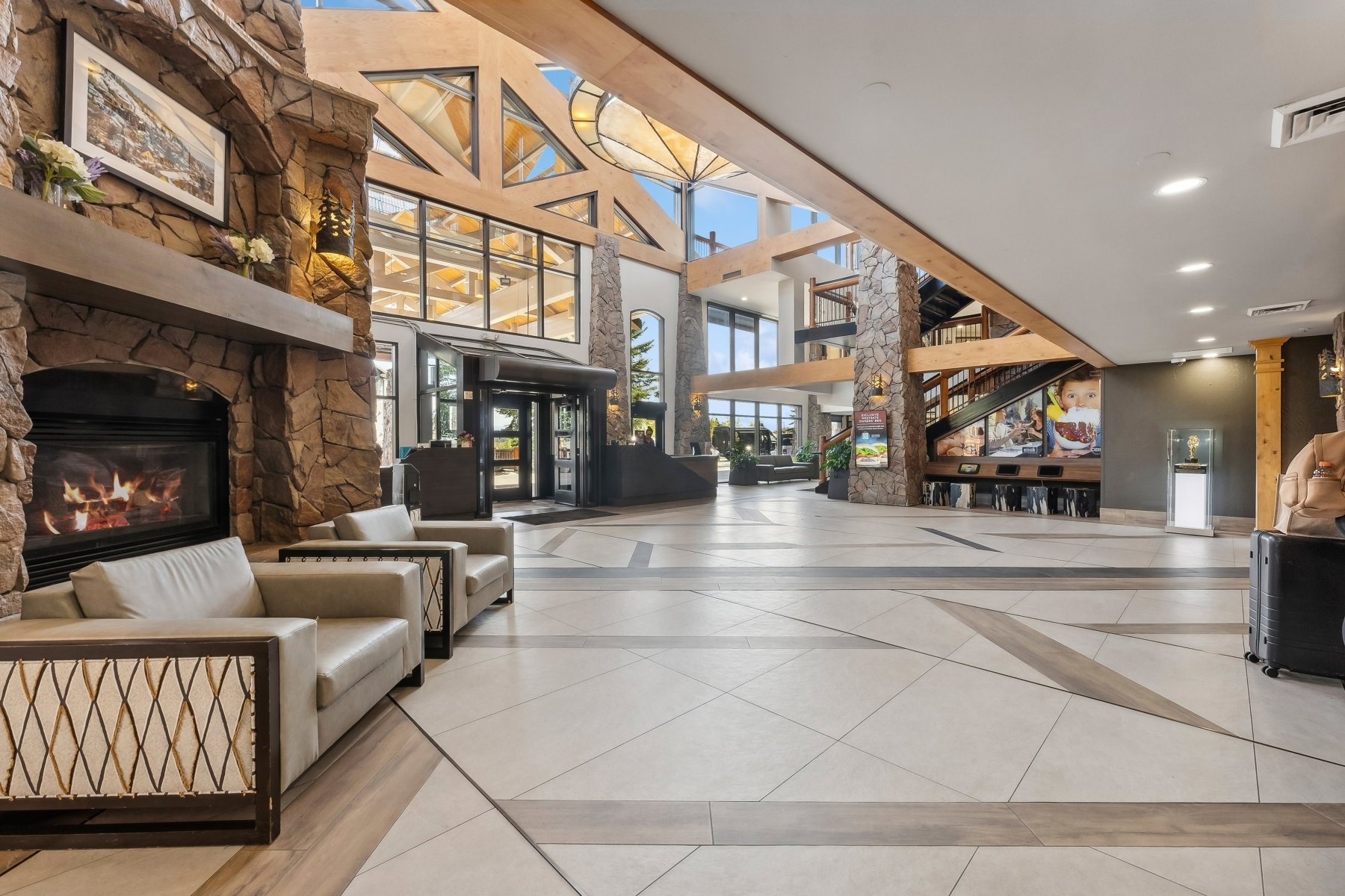 Spacious lobby featuring a stone-clad fireplace, soaring wood-beamed ceilings, geometric window designs, and large format tile flooring