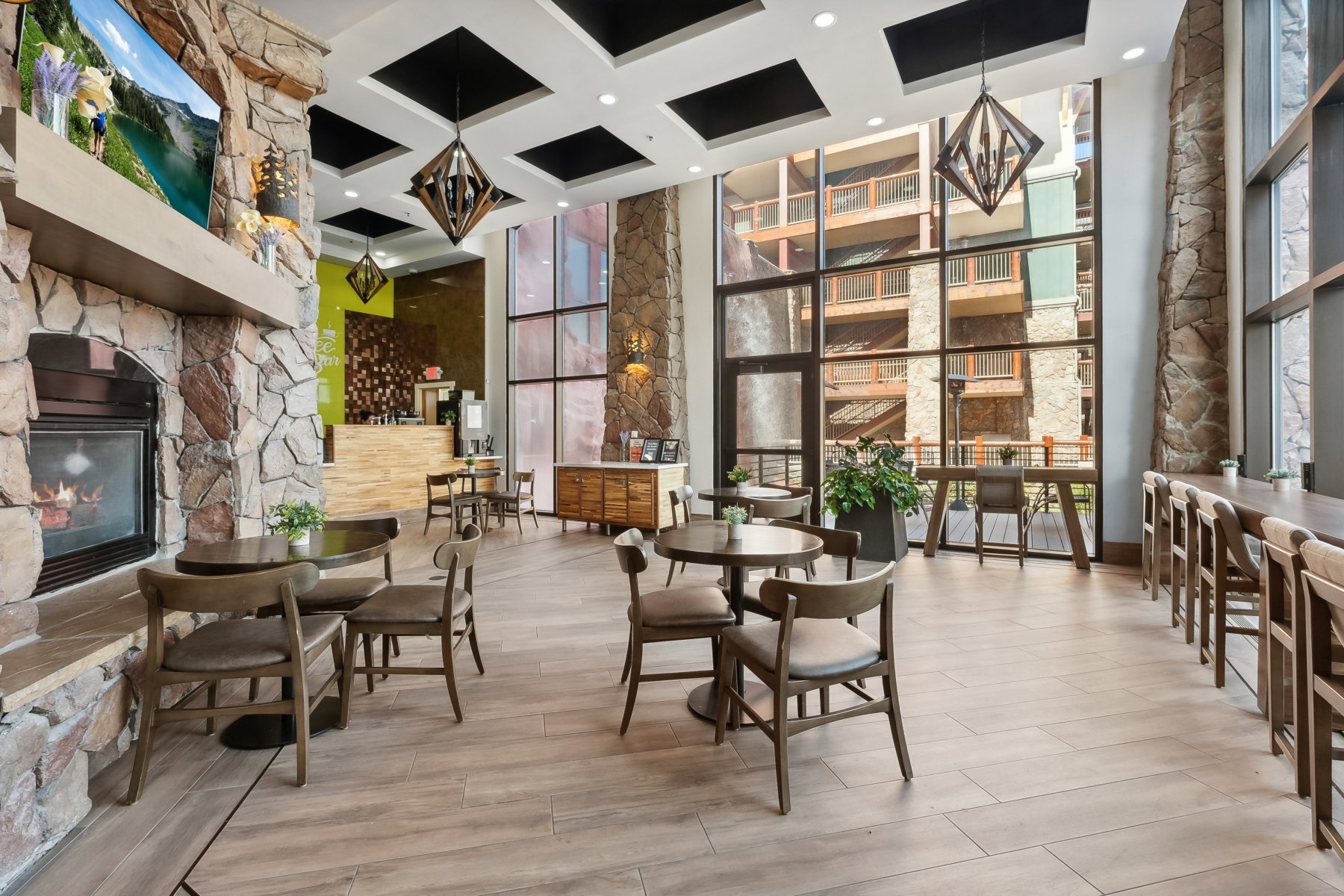 Spacious common area featuring a stone-clad fireplace, wood-finish flooring, a full-height window wall, and contemporary ceiling light fixtures