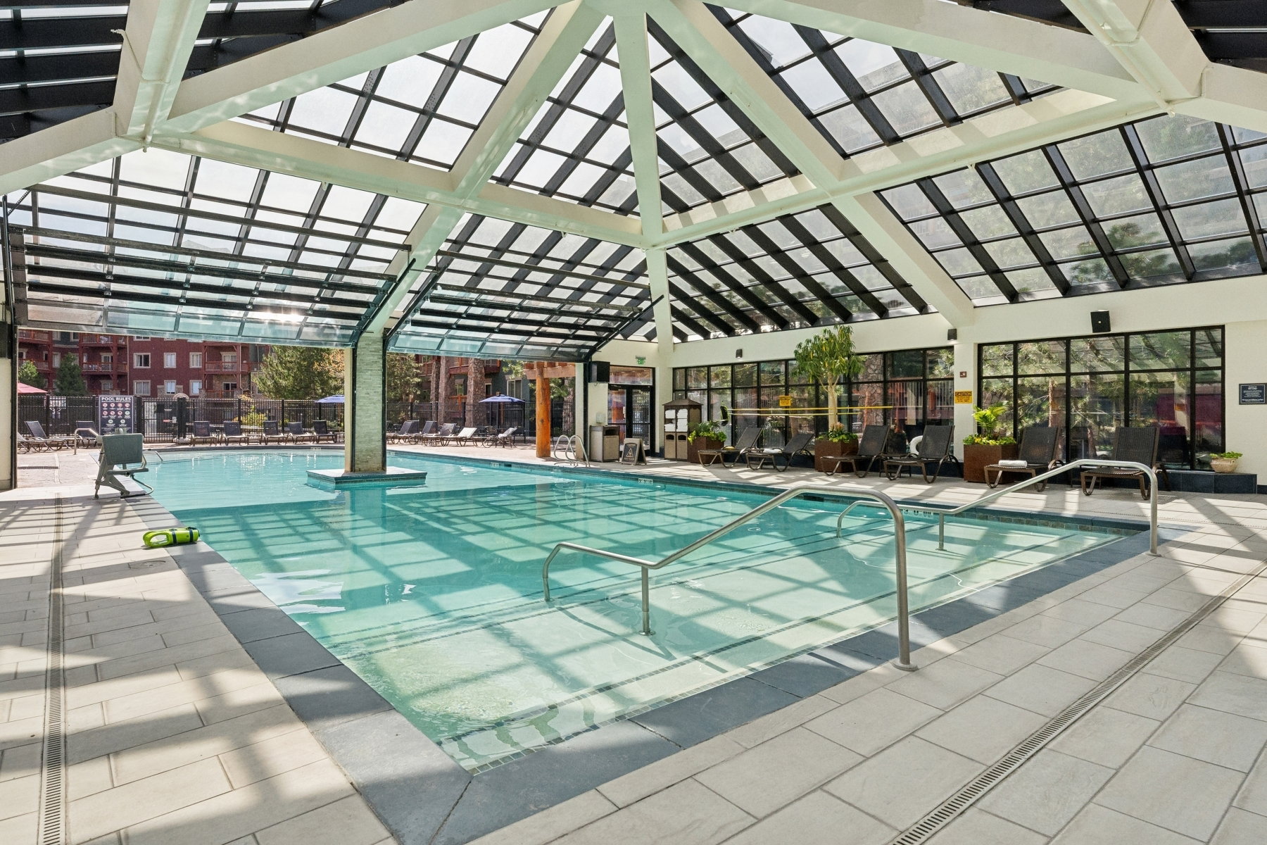 Indoor swimming pool featuring a vaulted glass ceiling and integrated hot tub