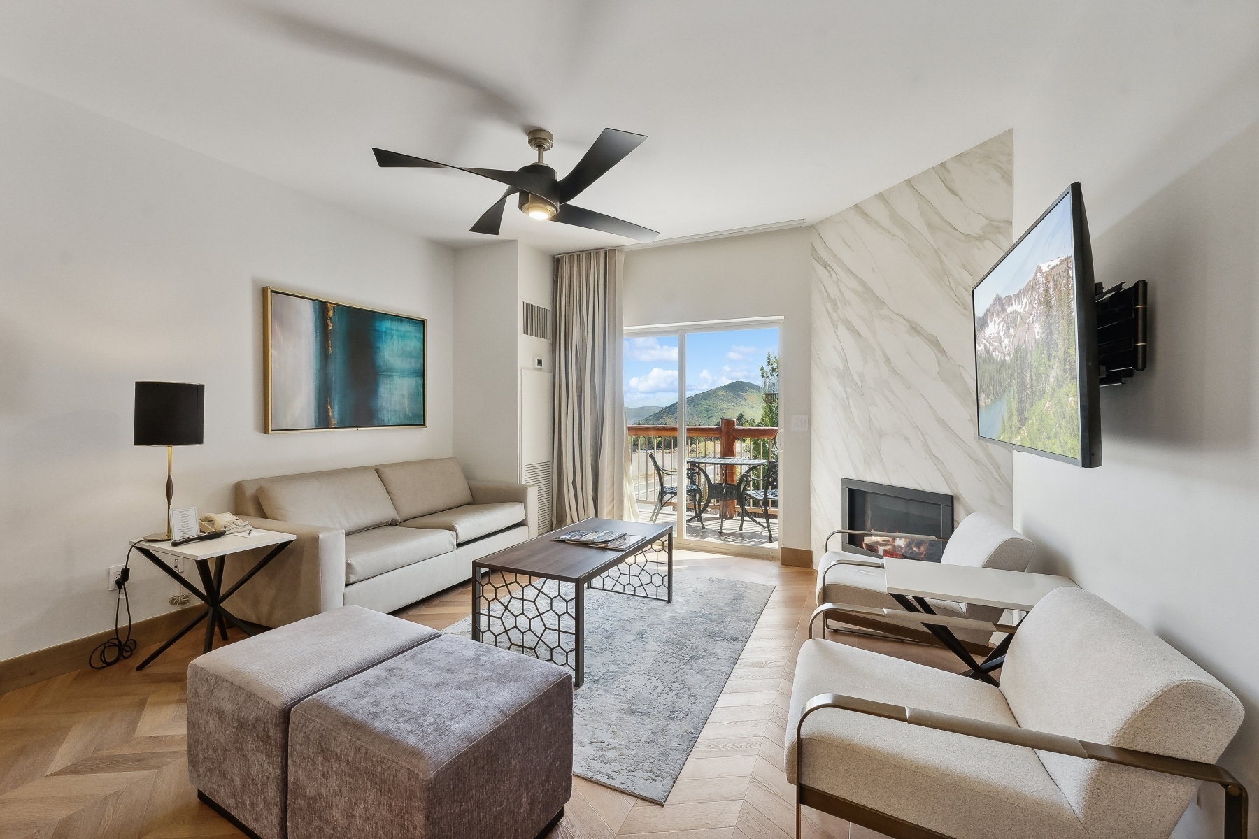 Living area with wood-finish herringbone flooring, a built-in fireplace featuring a stone-look surround, and a ceiling fan