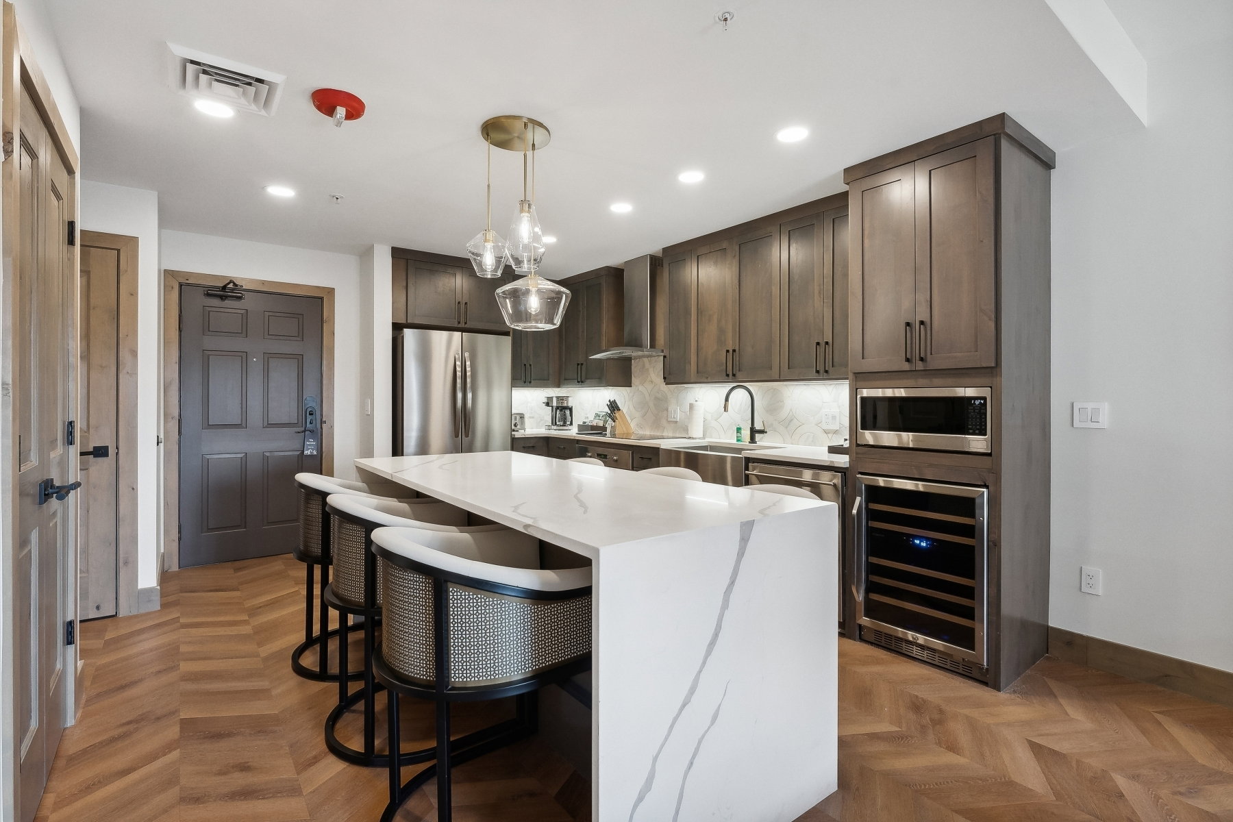 Kitchen featuring a waterfall island with stone countertop, herringbone wood-finish flooring, recessed lighting, and stainless steel appliances including a built-in microwave and wine refrigerator
