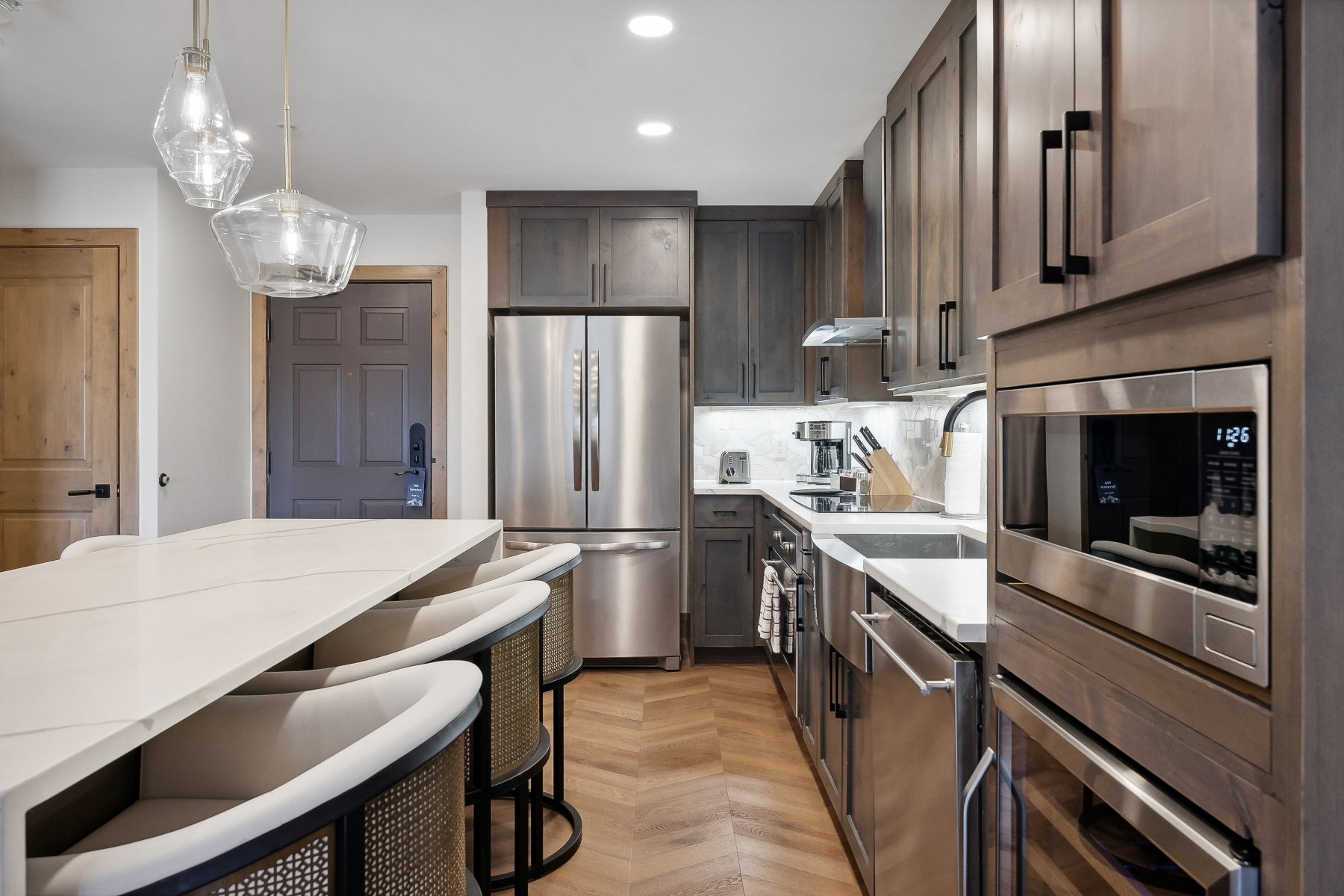 Gourmet kitchen featuring a built-in microwave, stainless steel appliances, wood-finish flooring, custom cabinetry, and an expansive island with a waterfall countertop