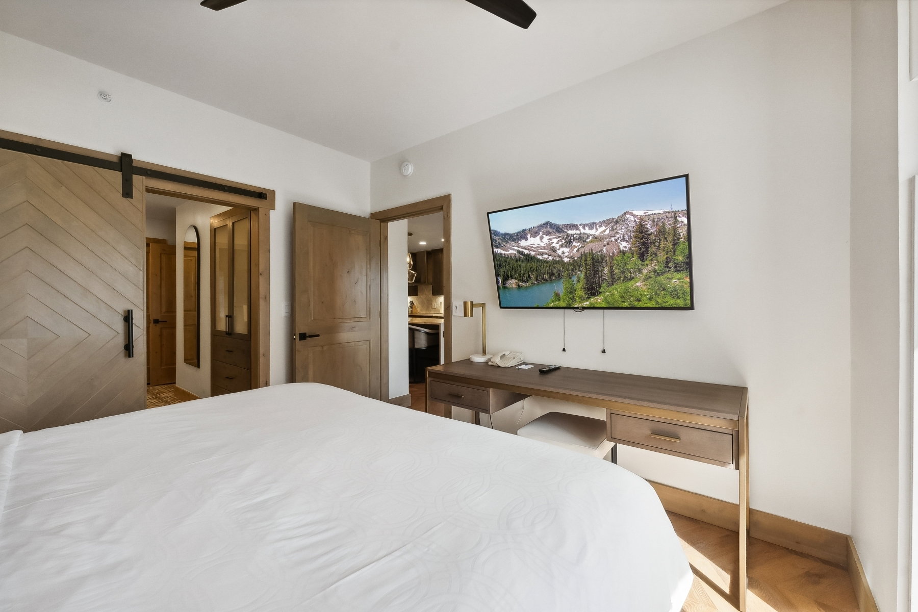 Bedroom featuring a chevron-patterned barn door, wood-finish flooring, a wall-mounted television, and a built-in desk with integrated storage
