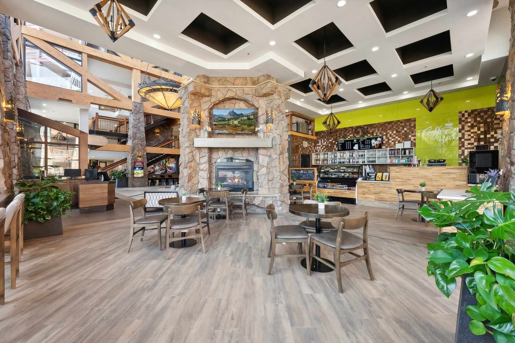 Spacious common area featuring a stone-clad fireplace and hearth, wood-finish flooring, a built-in service counter, recessed lighting, and decorative pendant light fixtures