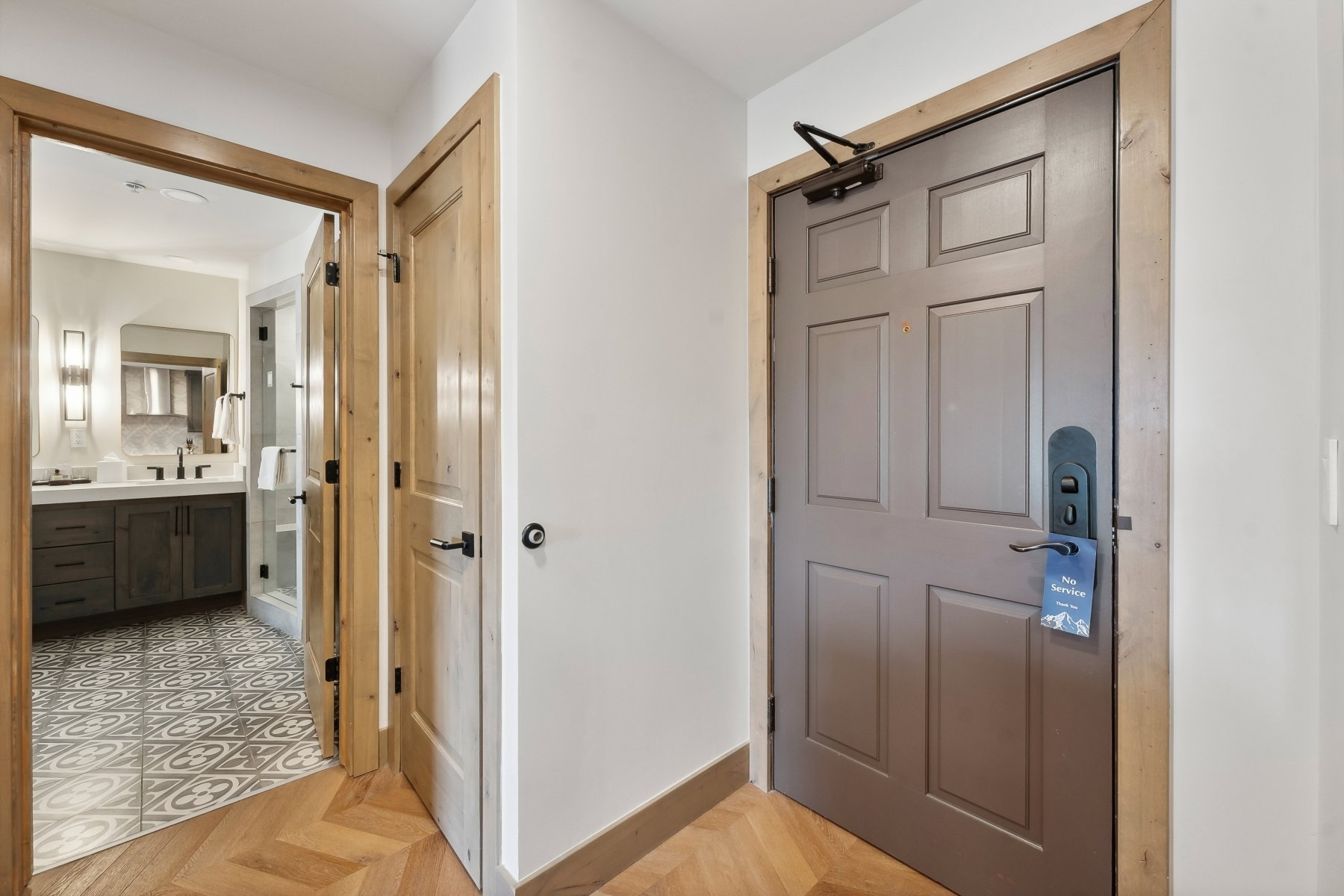 Herringbone wood-finish flooring extending into the hallway, featuring a panel-style entry door with modern hardware