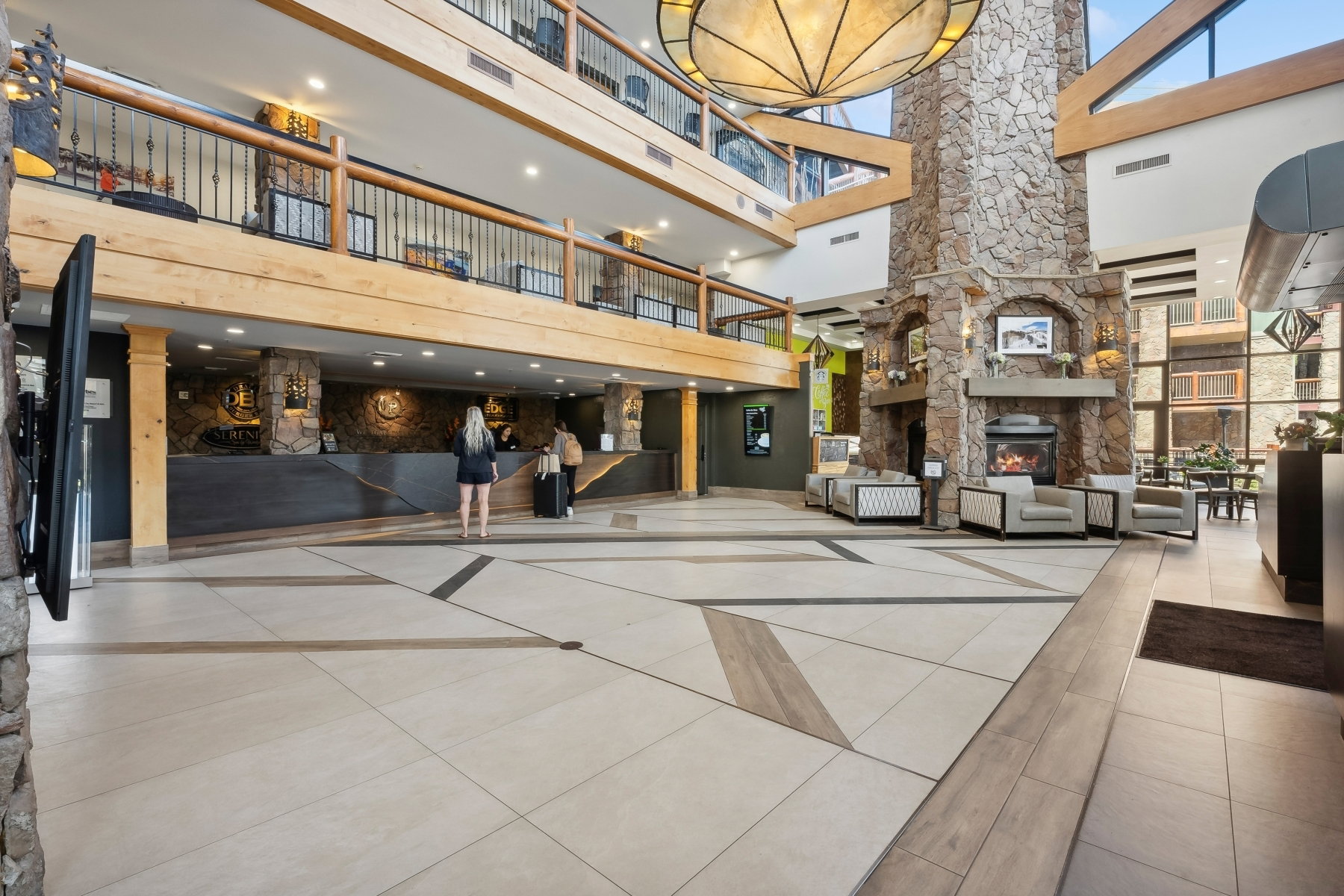 Grand foyer featuring a stone fireplace, integrated seating areas, and a multi-story atrium with exposed wood beams and wrought iron railings