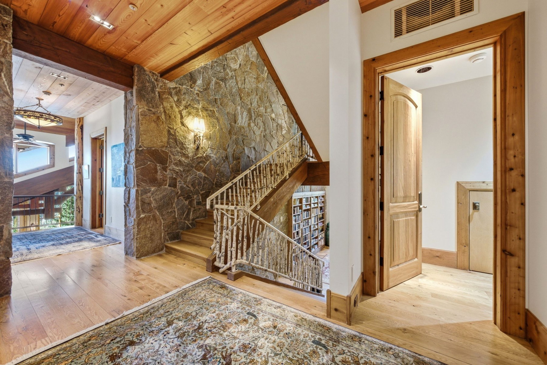 Stone accent wall featuring a wood-finish staircase with rustic twig-style railings